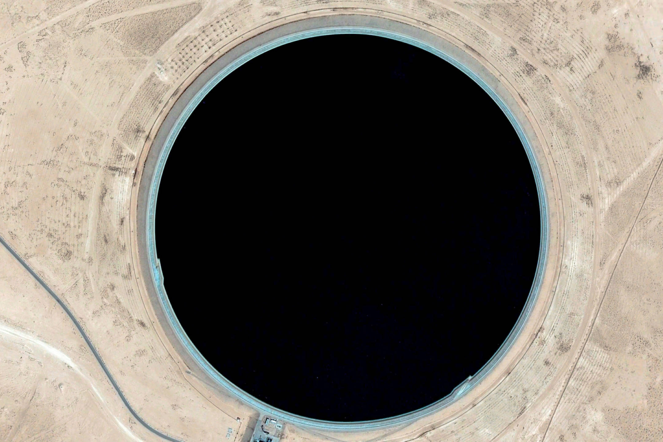 Google Earth 利比亞阿瓦特洞 壁紙 — 乾旱沙漠地形中一個巨大圓形水庫的鳥瞰圖，水色深黑。