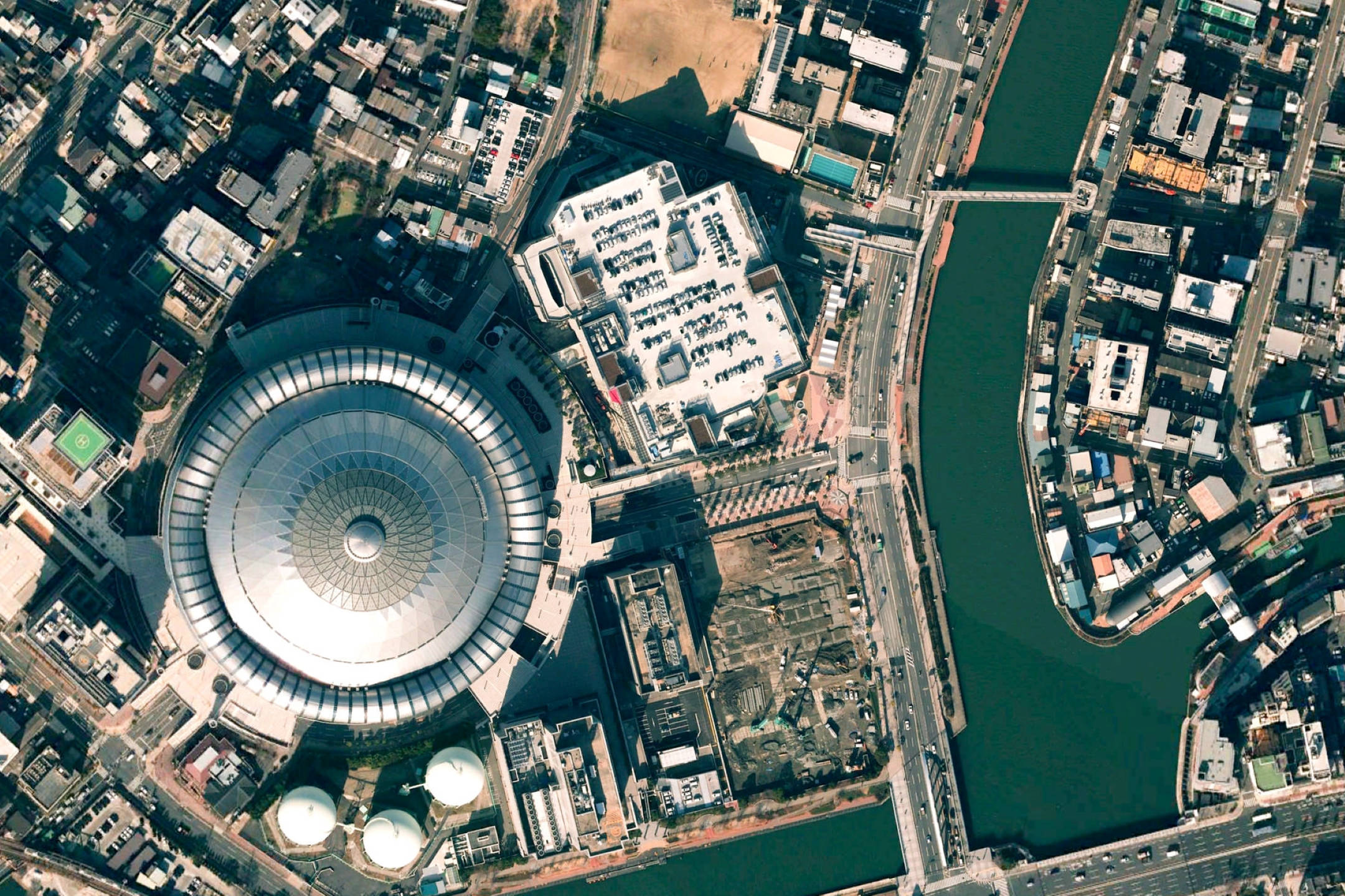 Google Earth 大阪京瓷巨蛋 壁紙 — 俯瞰一個大型圓頂體育館，坐落於城市建築物和蜿蜒河流之間。