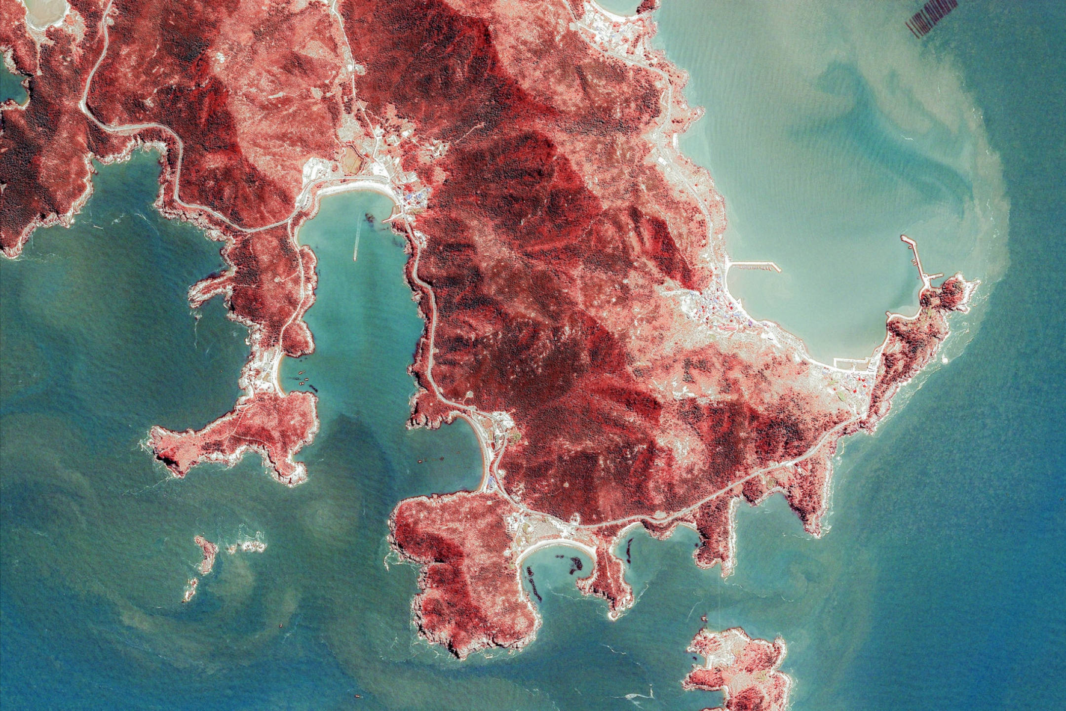 Google Earth韓國釜山海岸 壁紙 — 崎嶇的紅土海岸線延伸至碧綠海水，蜿蜒的白色道路縱橫其間的鳥瞰圖。