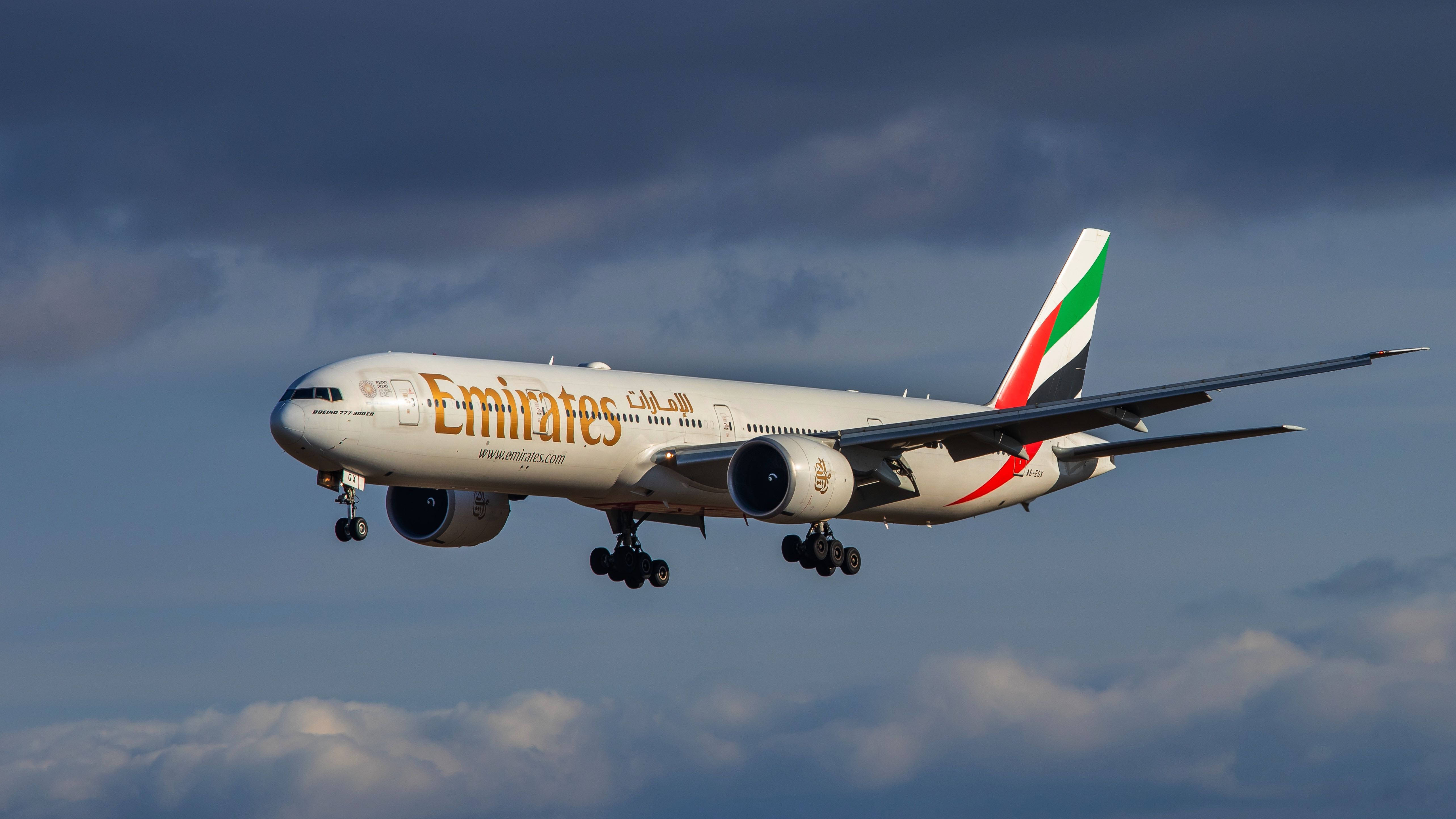 Google Flights 上的阿聯酋客機空中飛行 壁紙 — 阿聯酋航空飛機在戲劇性的多雲天空下降落，起落架已放下。