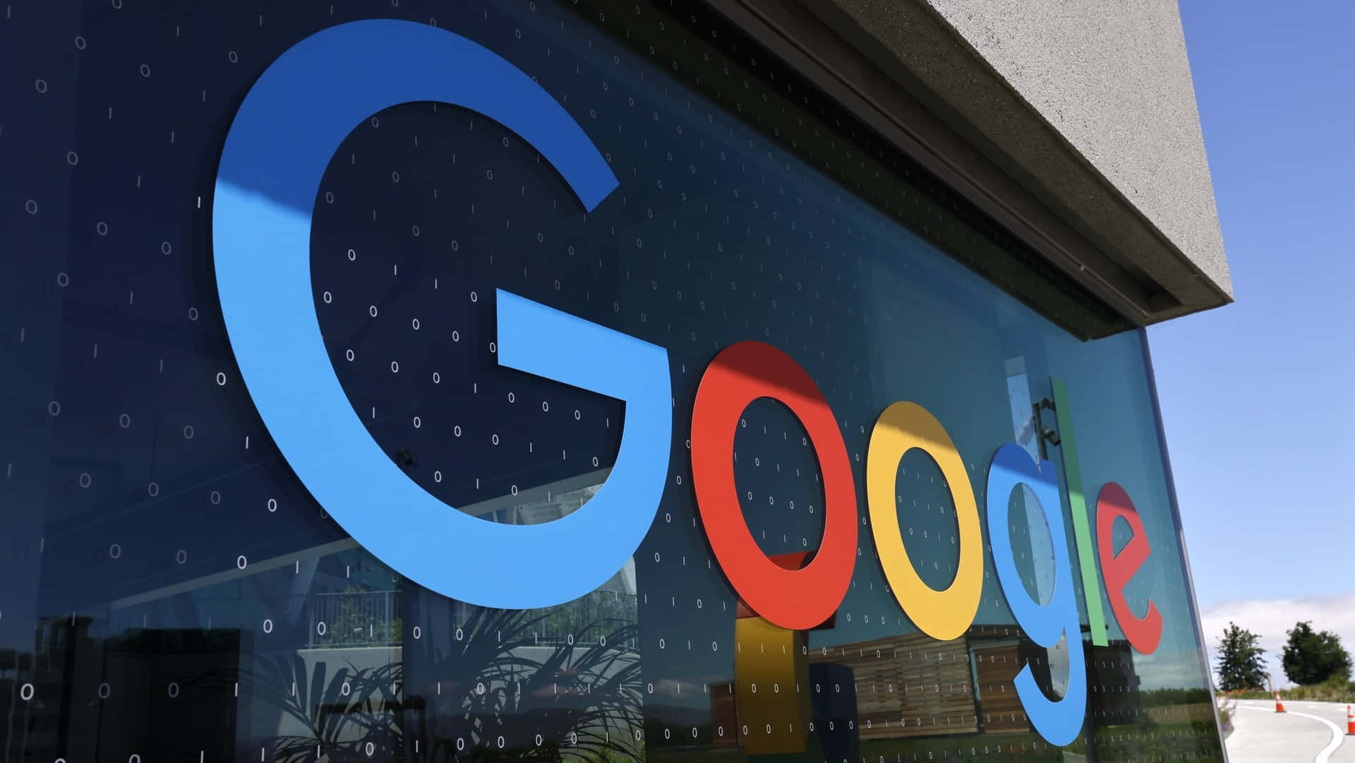 玻璃建築上的Google標誌，帶有二進制代碼圖案和天空倒影。