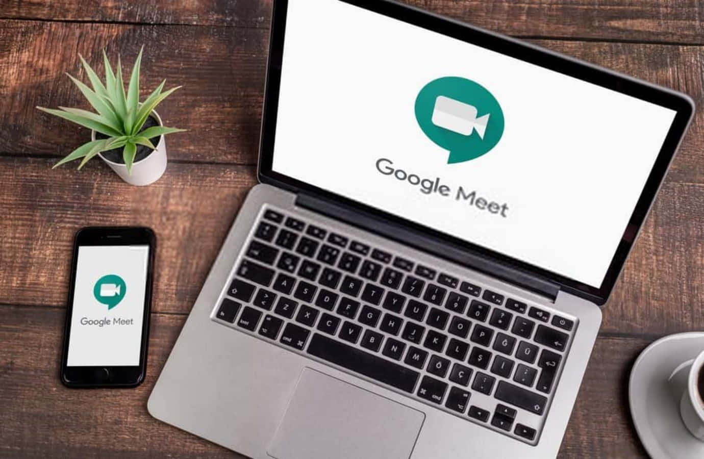 Google Meet 虛擬協作 壁紙 — 一部手提電腦和智能手機在質樸的木桌上顯示 Google Meet 應用程式，旁邊有一盆植物和一杯咖啡。