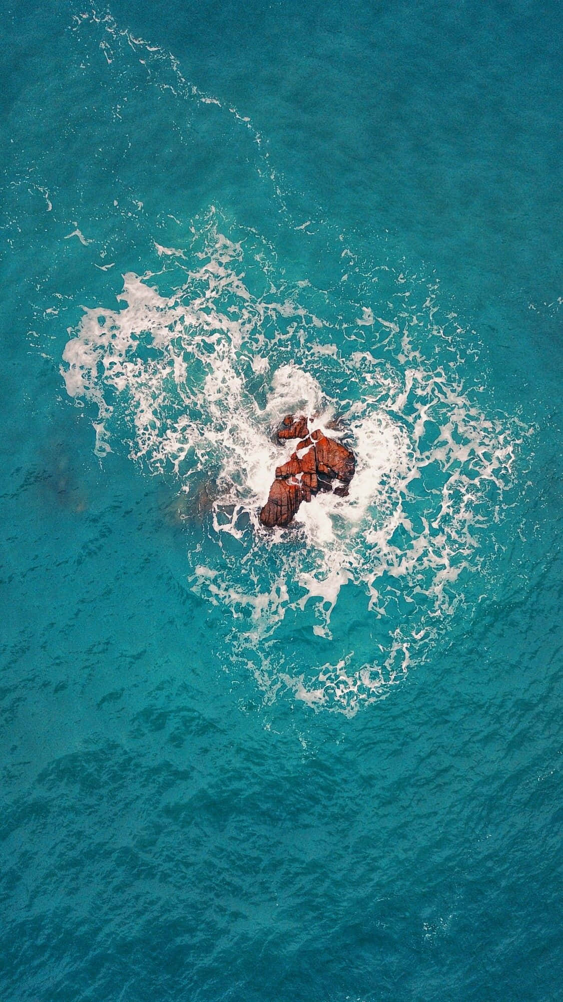 Google Pixel 海島鳥瞰圖 壁紙 — 從高空俯瞰，碧綠的海浪拍打著崎嶇的紅褐色岩石形成。
