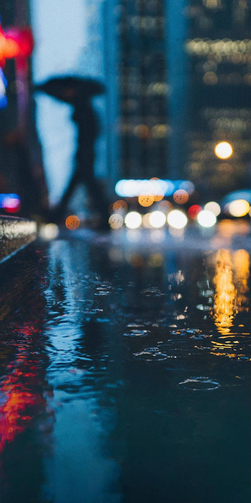 撐傘人物的剪影在夜晚雨中城市行走，伴隨著發光的倒影。