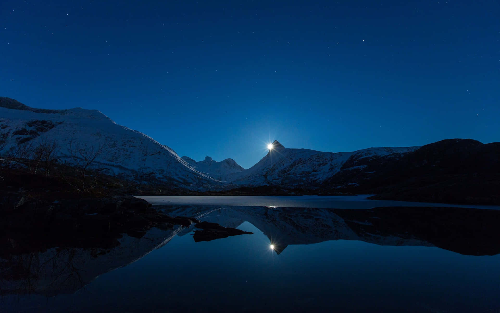 白雪覆蓋的山峰在星光下閃耀，倒映在夜晚平靜的湖面上。