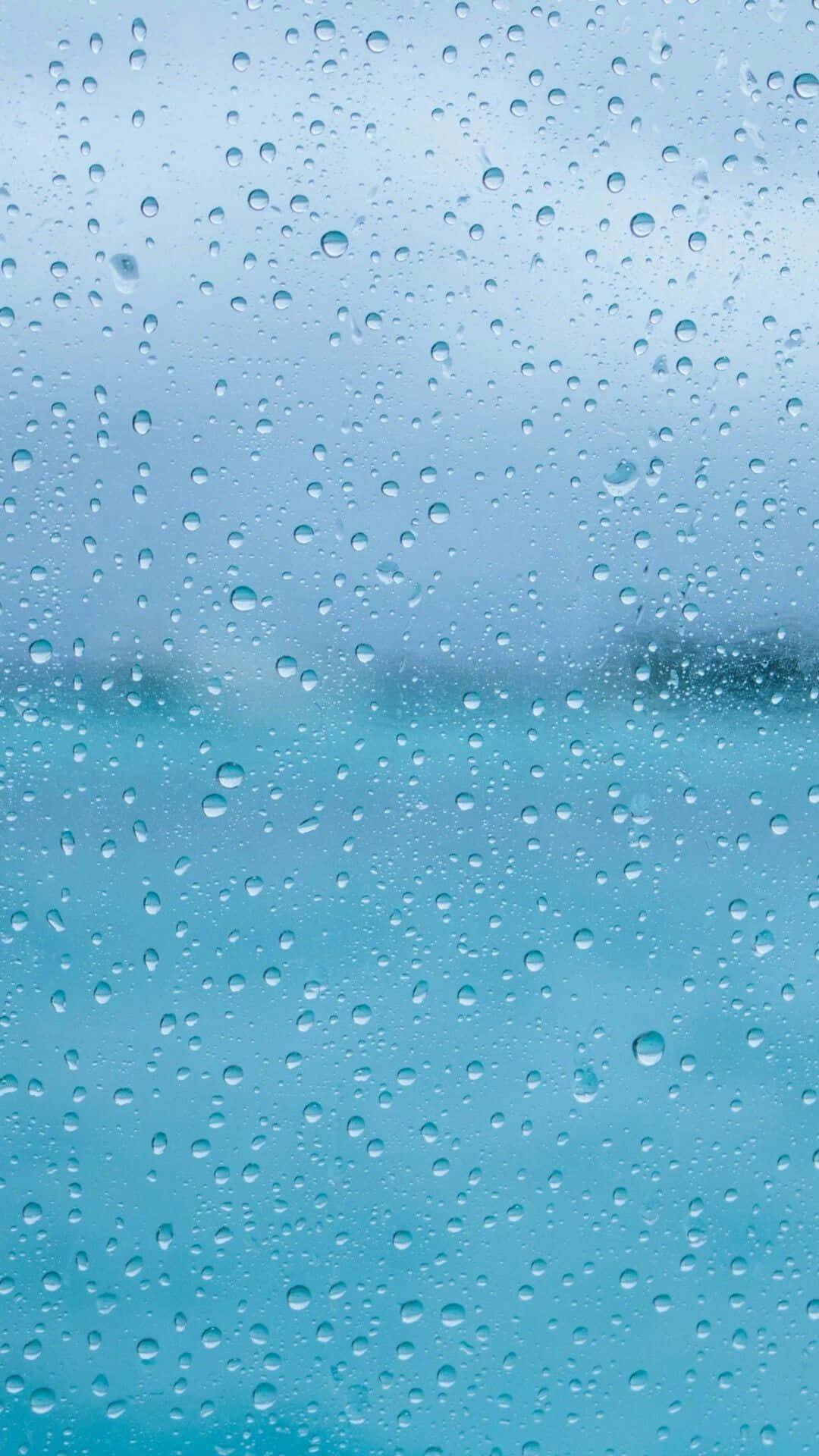 玻璃上的雨滴與模糊的藍色海洋和天空景觀