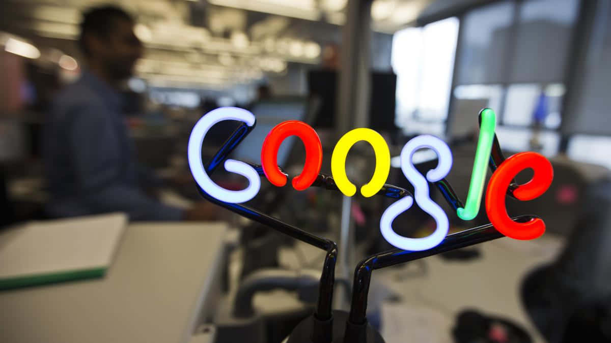 現代辦公室桌上的霓虹Google標誌，後面有模糊的員工。