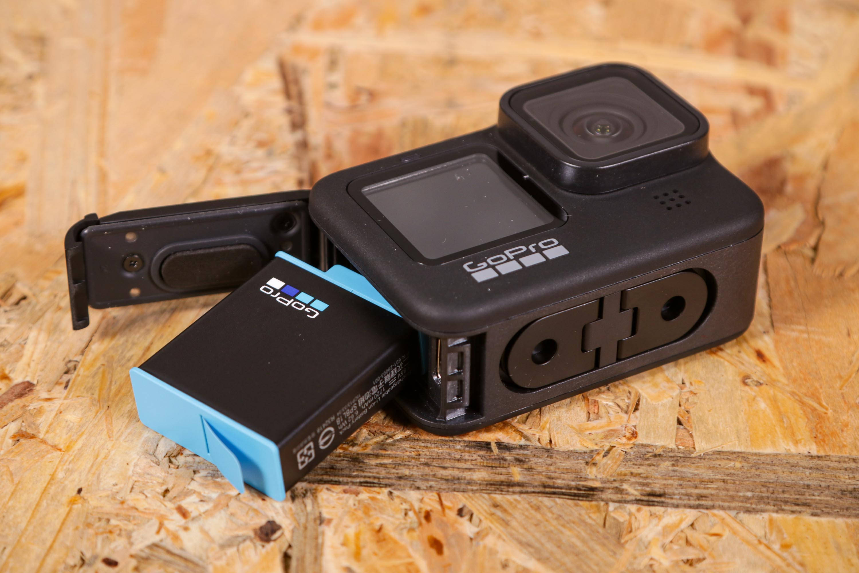 GoPro Hero 9 Black 增強電池續航力，拍攝更持久 壁紙 — 一部黑色GoPro運動相機連同分離的電池放置在顯示木紋的紋理夾板上。