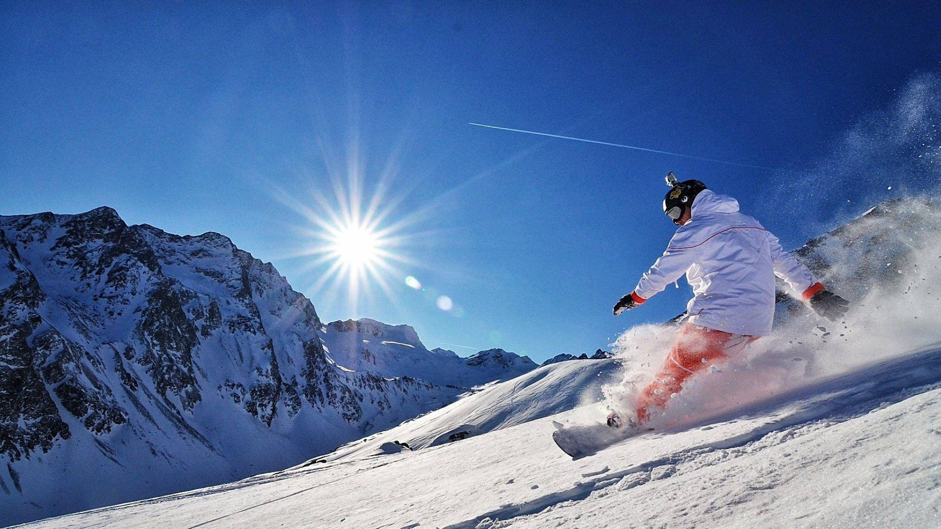 GoPro 拍攝的滑雪板滑行者 壁紙 — 一名滑雪板運動員在陽光照耀的雪坡上 carving，背景是山脈和明亮的藍天。