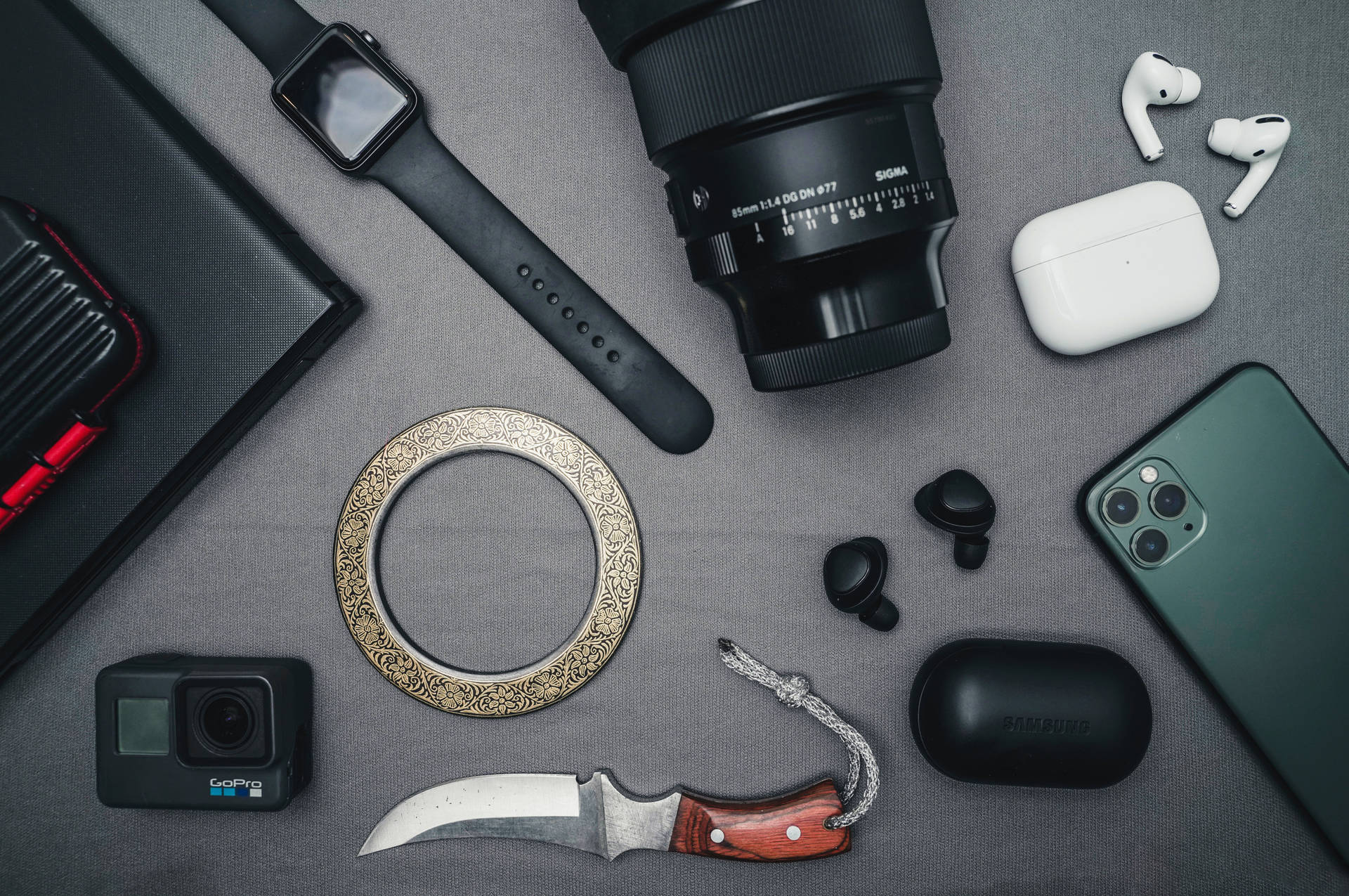 GoPro冒險體驗 壁紙 — 在紋理灰色表面上平鋪擺放現代科技小工具和裝飾刀。