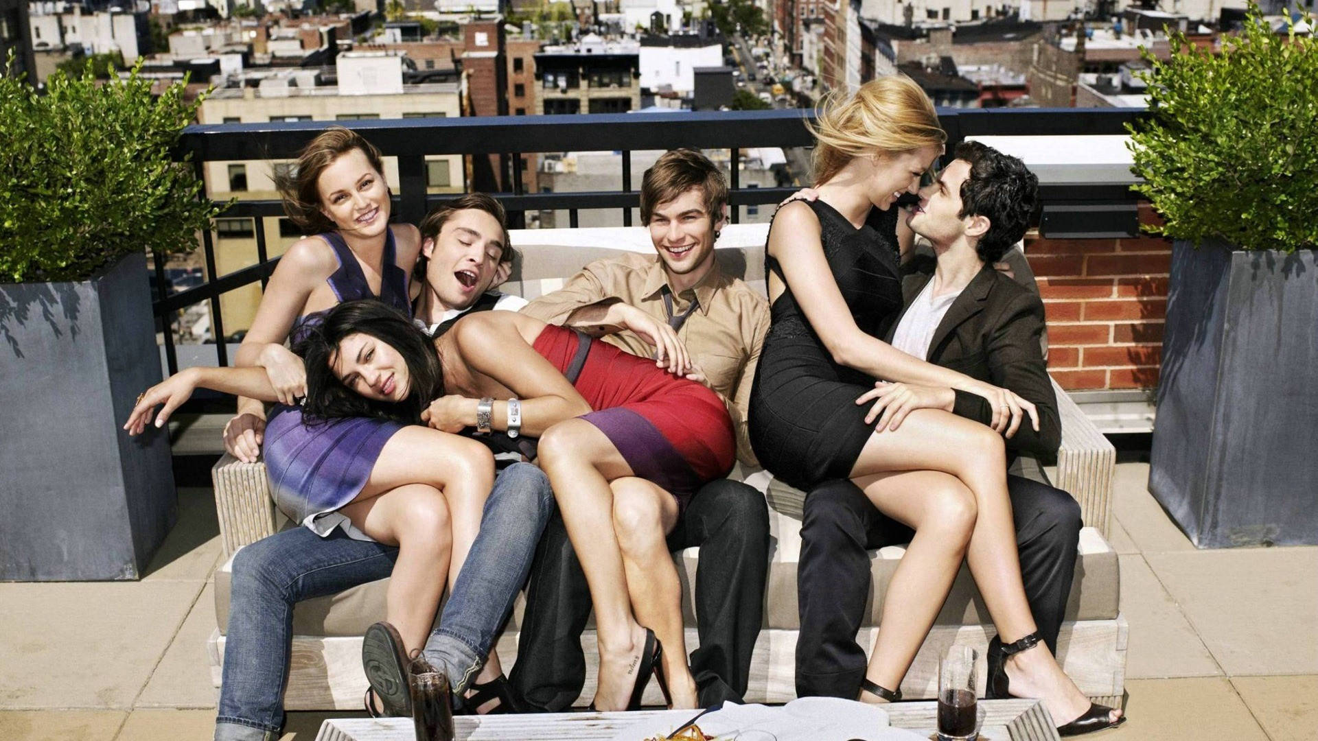 Gossip Girl 屋頂聚會 壁紙 — 六位朋友在陽光普照下，於屋頂酒廊歡笑放鬆，背景是城市天際線。