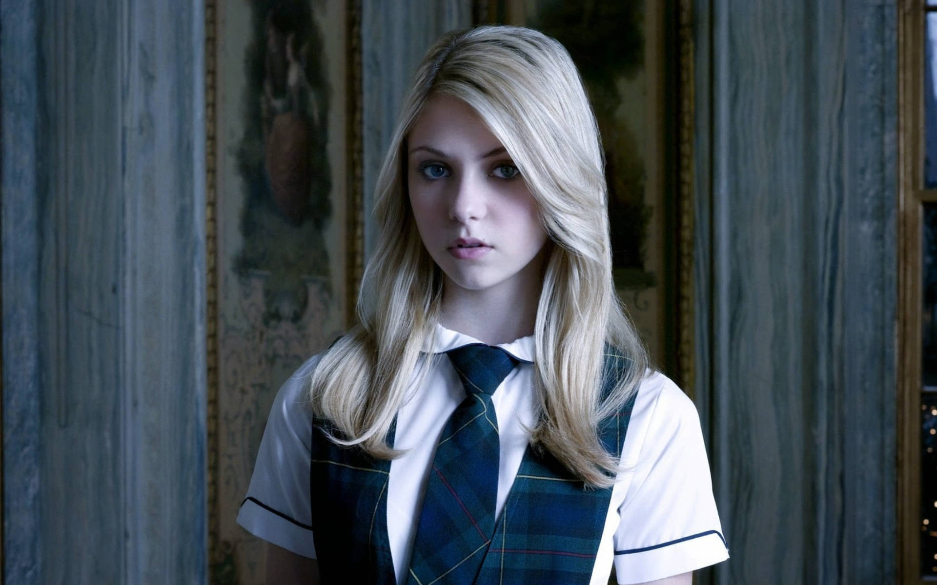 《Gossip Girl》珍妮·漢弗萊 壁紙 — 一位金髮女孩穿著校服，搭配格子背心和領帶，站在一個光線昏暗、裝飾華麗、有大理石牆壁的房間裡。