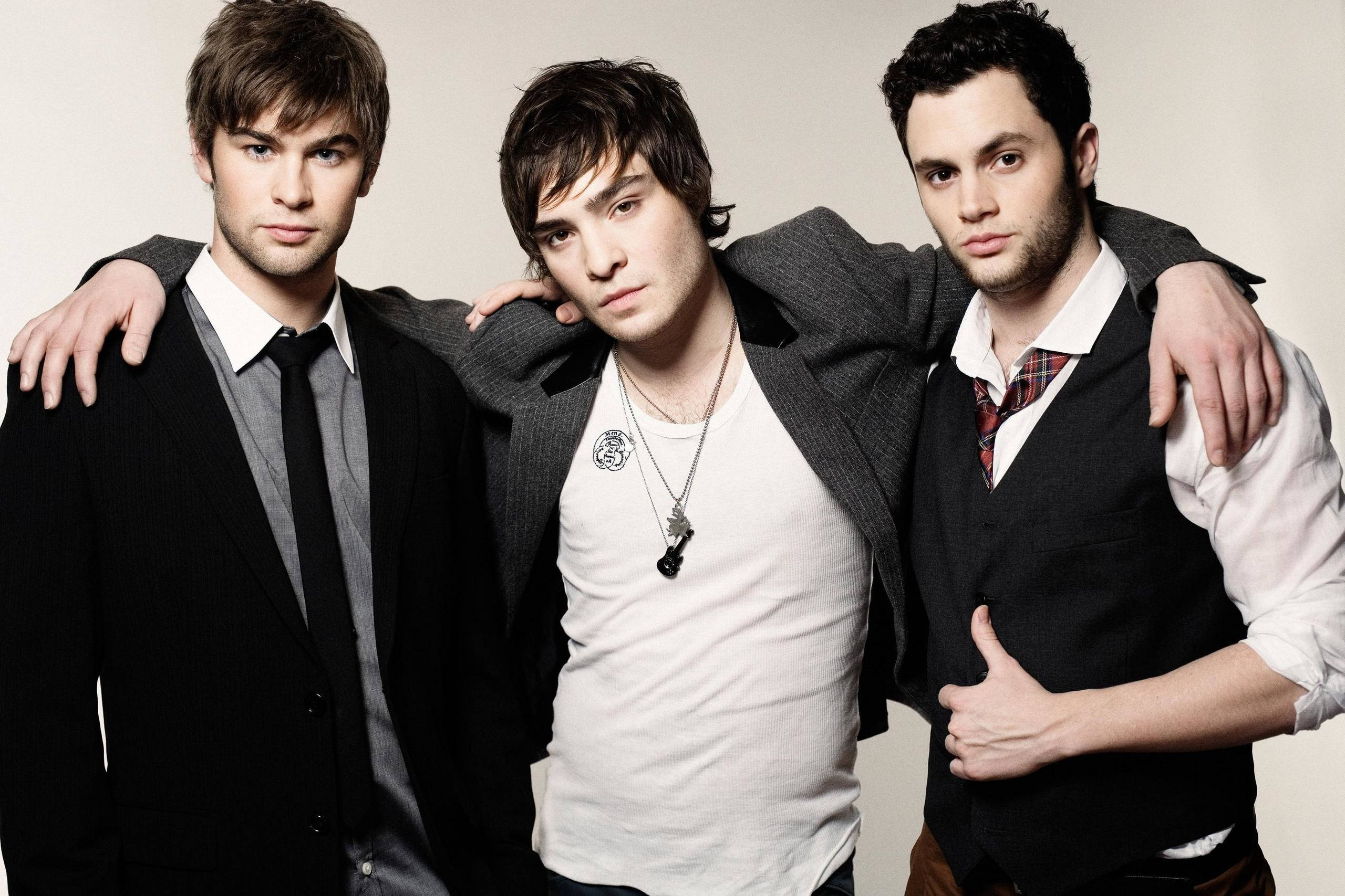 Gossip Girl 男演員群像 壁紙 — 三位年輕男士穿著時尚休閒服，在純色攝影棚背景前緊密地互相搭肩擺姿勢。