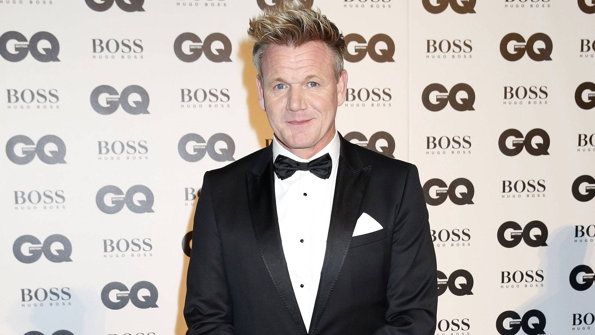 戈登·拉姆齊 GQ 與 Hugo Boss 壁紙 — 戈登·拉姆齊身穿利落的黑色燕尾服搭配領結，自信地站在重複的GQ和Hugo Boss品牌背景前。
