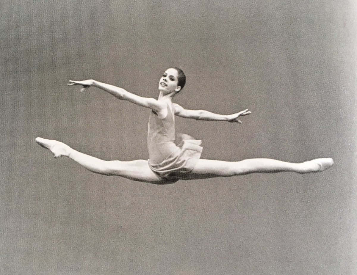 Darcey Bussell 桌布 壁紙 — 一位優雅的芭蕾舞者，在純灰色工作室背景前，被捕捉到空中完美劈腿跳躍的瞬間。