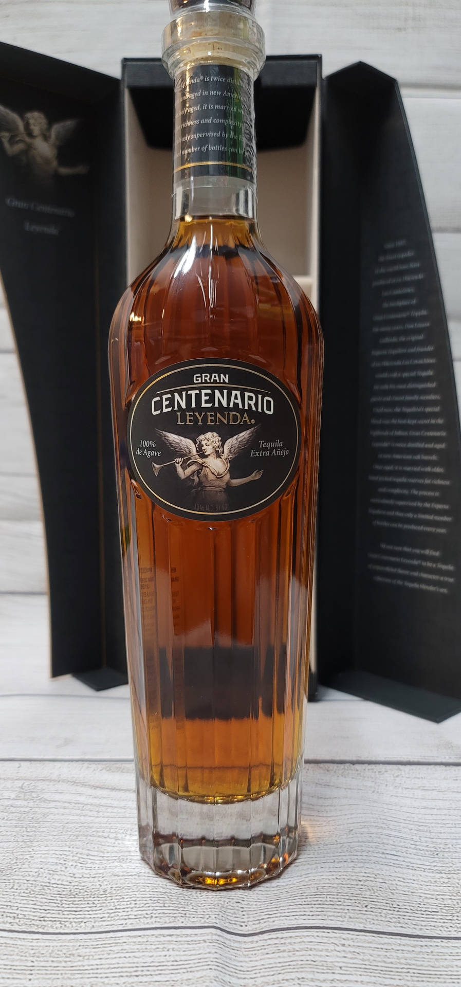一瓶Gran Centenario Leyenda龍舌蘭酒放在木質表面上，旁邊有黑色盒子。