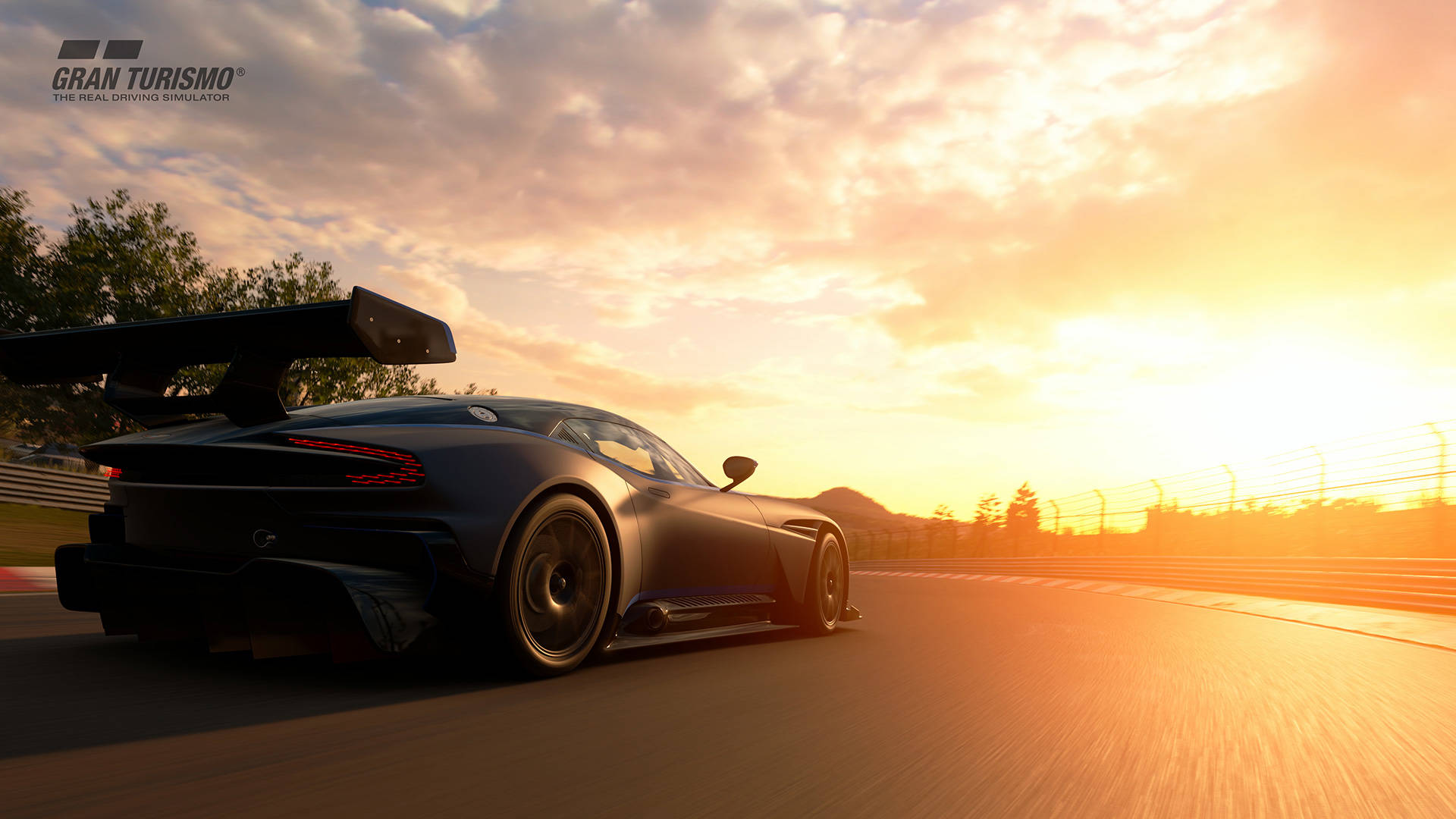 《Gran Turismo》遊戲中的運動跑車 4K 壁紙 — 一輛時尚的黑色賽車，帶有大型後翼，在日落時分沿著賽道飛馳，將金色光芒灑在瀝青路面上。
