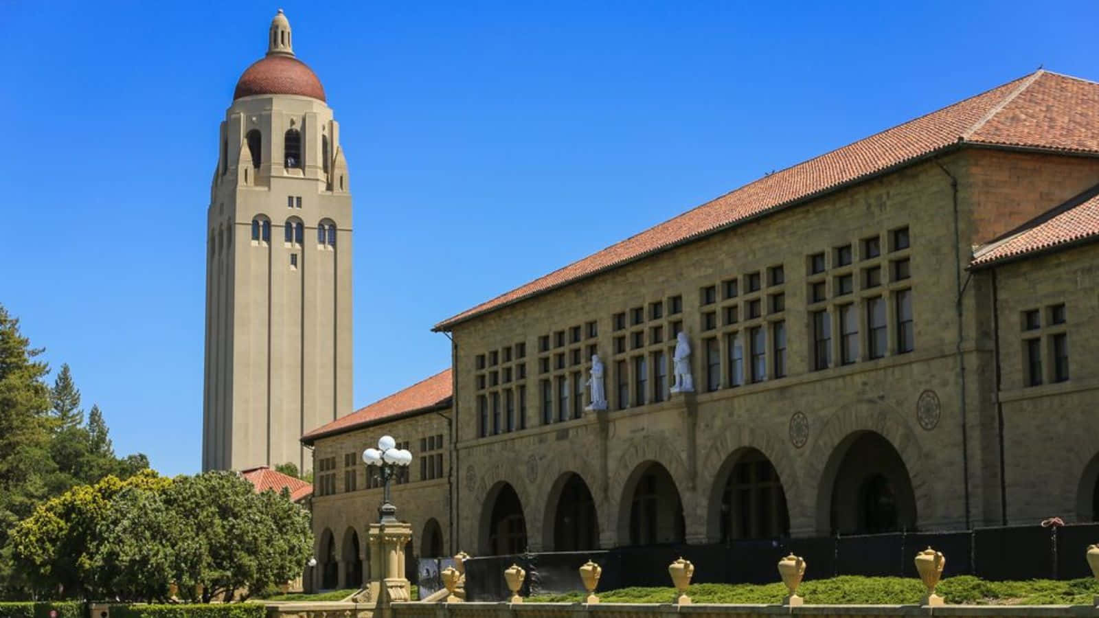  壁紙 — 一座宏偉的米黃色大學建築，擁有高高的鐘樓和紅色瓦片屋頂，在清澈的藍天下。