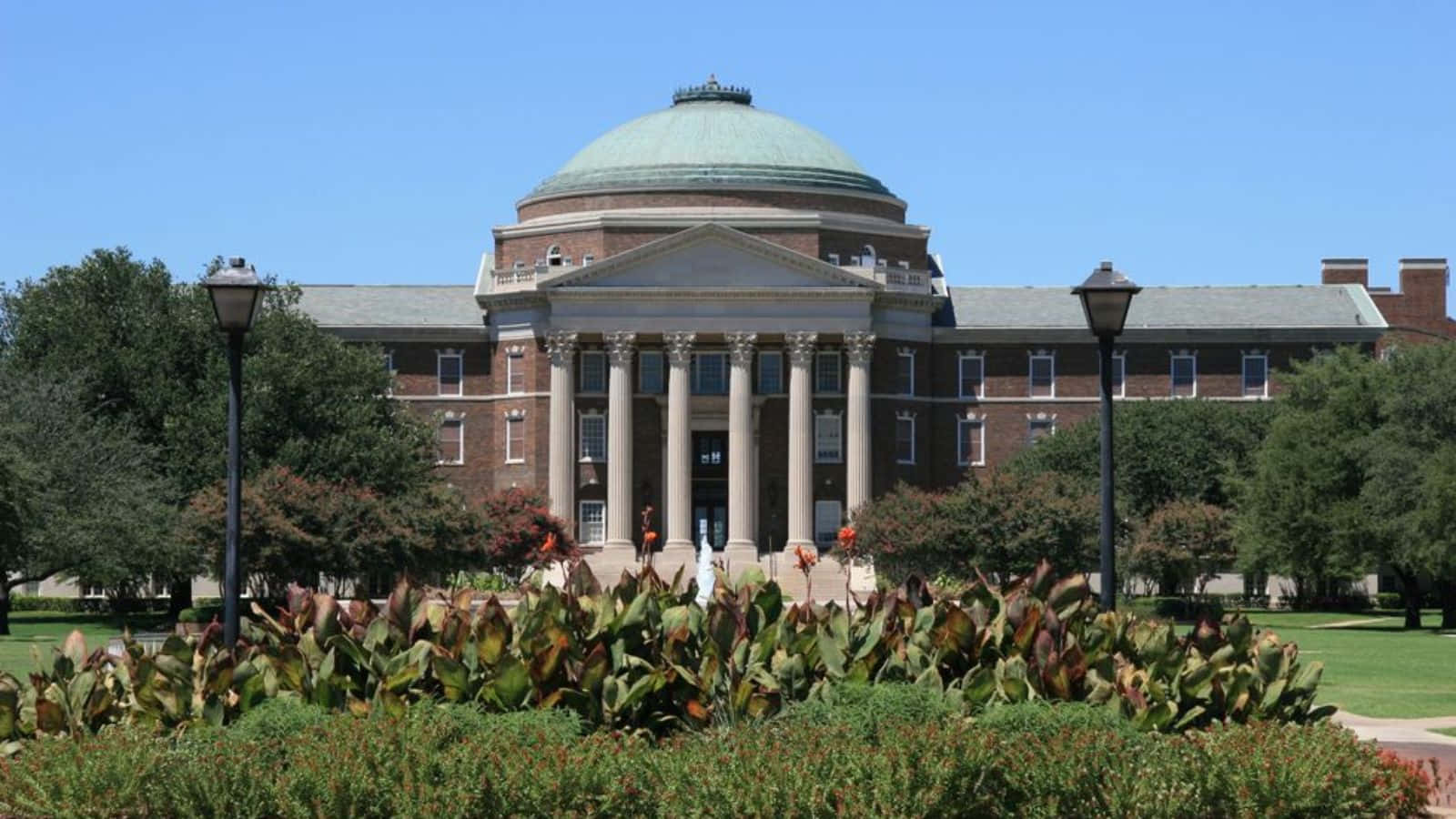  壁紙 — 一座宏偉的新古典主義大學建築，擁有綠色圓頂和柱子，矗立在晴朗的藍天下，周圍是修剪整齊的花園和樹木。