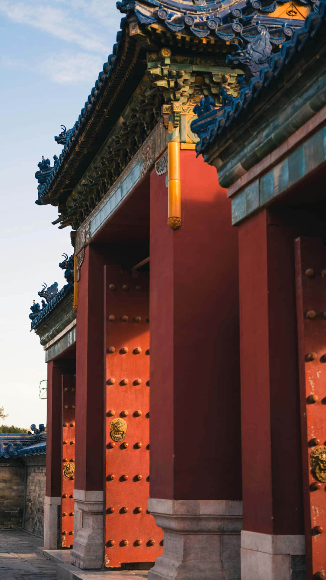  壁紙 — 一座宏偉的傳統中式大門，配有紅色門扉、金色裝飾和藍色瓦片屋頂，沐浴在溫暖的金色光輝中。