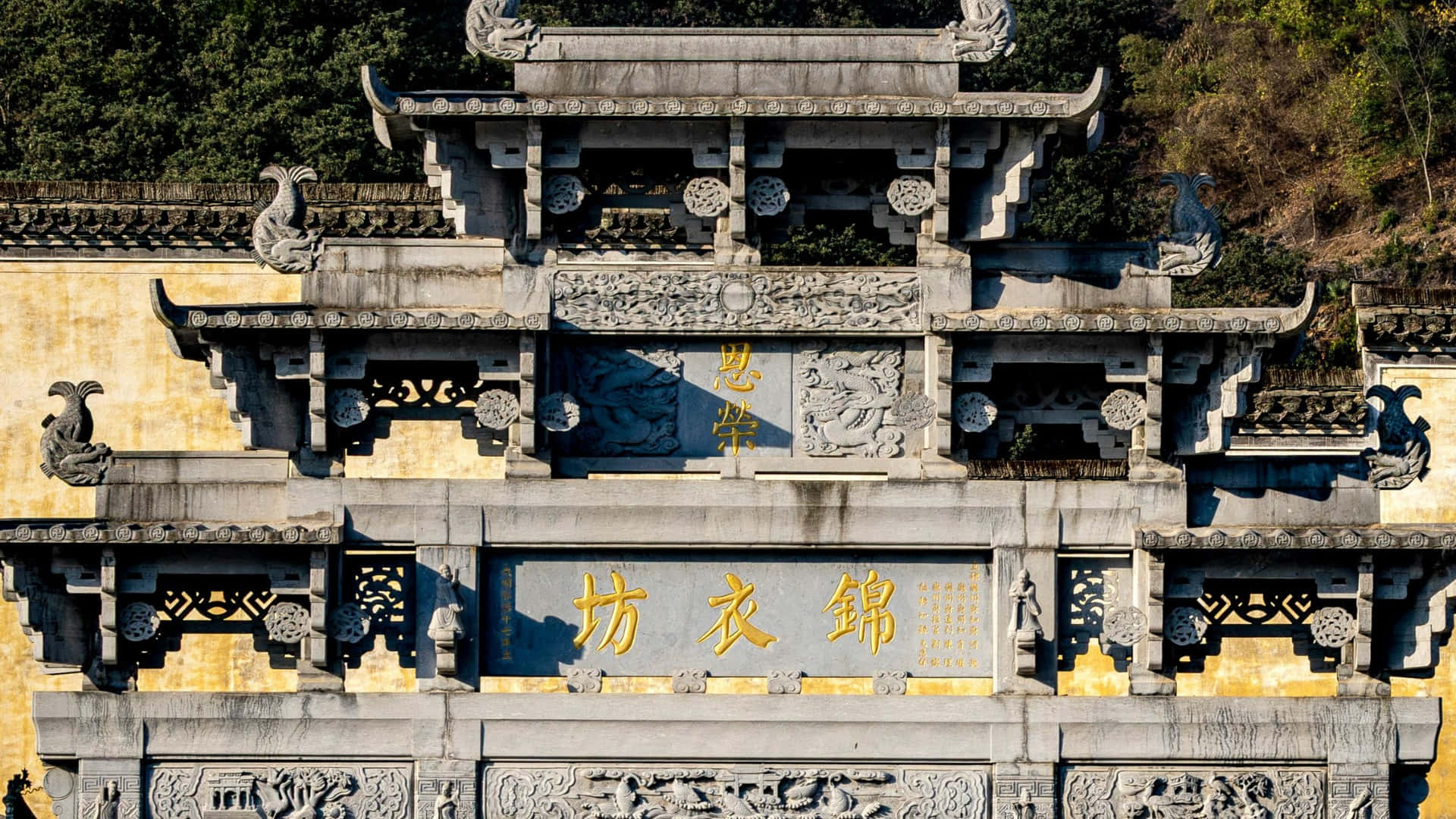  壁紙 — 一座宏偉的傳統中式石牌坊，帶有精緻的雕刻、金色文字和華麗的屋頂細節，沐浴在明亮的日光下。