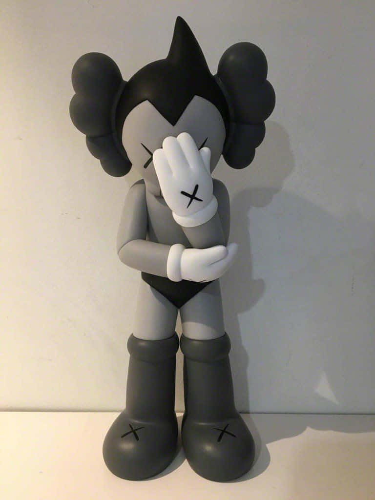 Kaws Astro Boy 桌布 壁紙 — 一個灰色和黑色的KAWS Companion搪膠公仔站立，一隻手遮住臉，靠著純白牆壁。