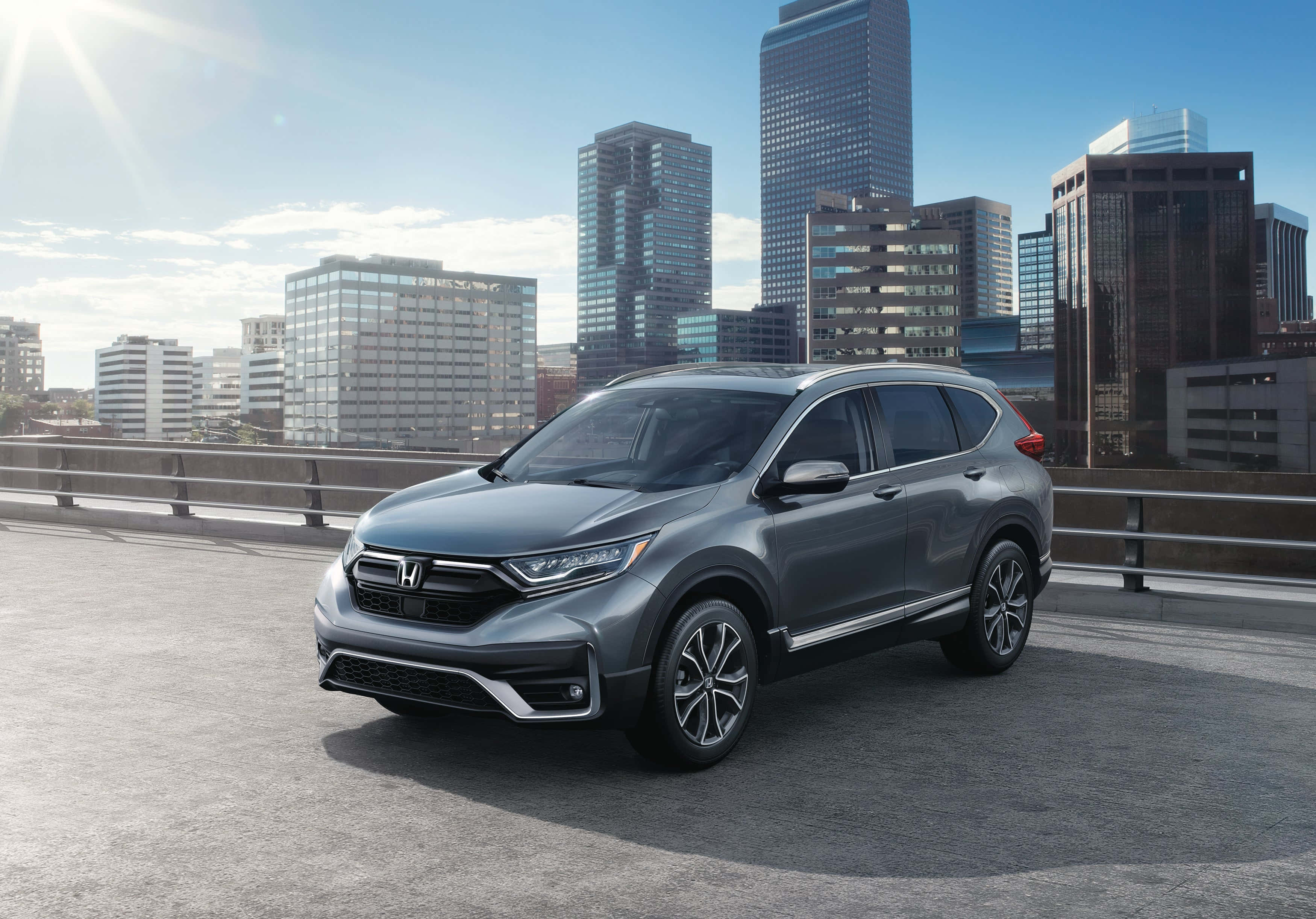 Honda Cr-v 桌布 壁紙 — 一架流線型灰色本田CRV在陽光明媚的橋上行駛，背景是現代城市天際線。