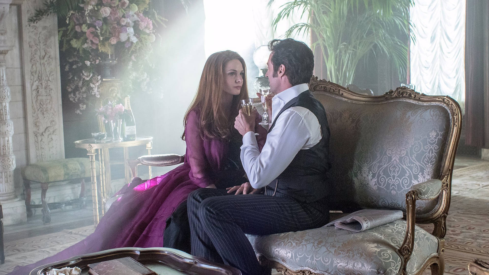 《 Greatest Showman 》室內情侶 壁紙 — 一男一女身穿優雅的時代服裝，坐在陽光普照的豪華客廳中一張華麗的沙發上，分享親密時刻。