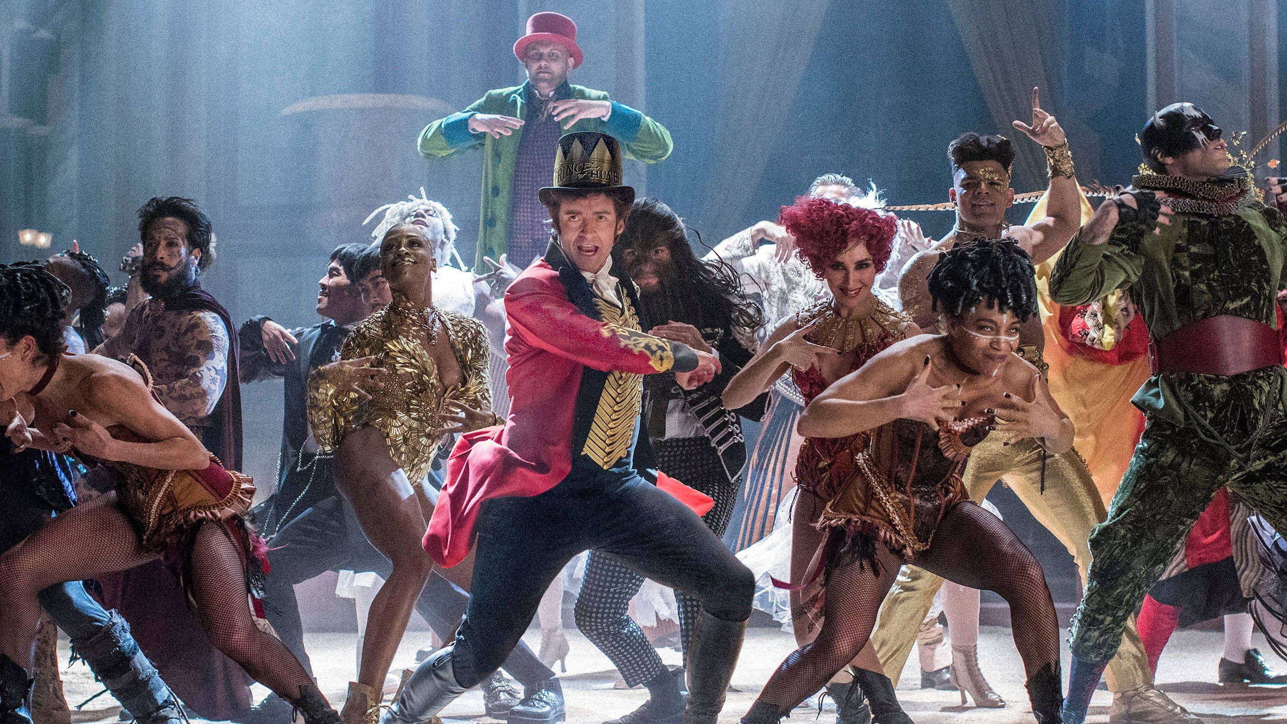 《 Greatest Showman 》表演對決 壁紙 — 一個充滿活力的劇團穿著華麗的服裝，在戲劇性的舞台燈光下充滿活力地跳舞。
