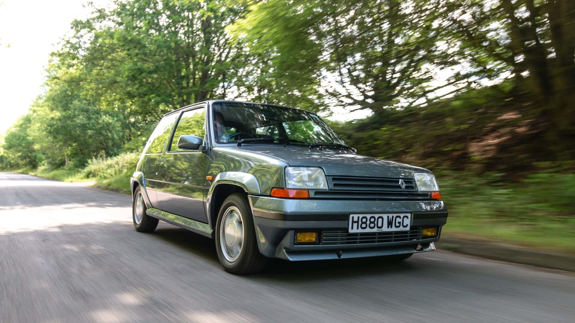 Renault 5 Turbo 桌布 壁紙 — 一輛綠色雷諾5 Turbo在陽光明媚的森林道路上疾馳，樹木呈現動態模糊效果。