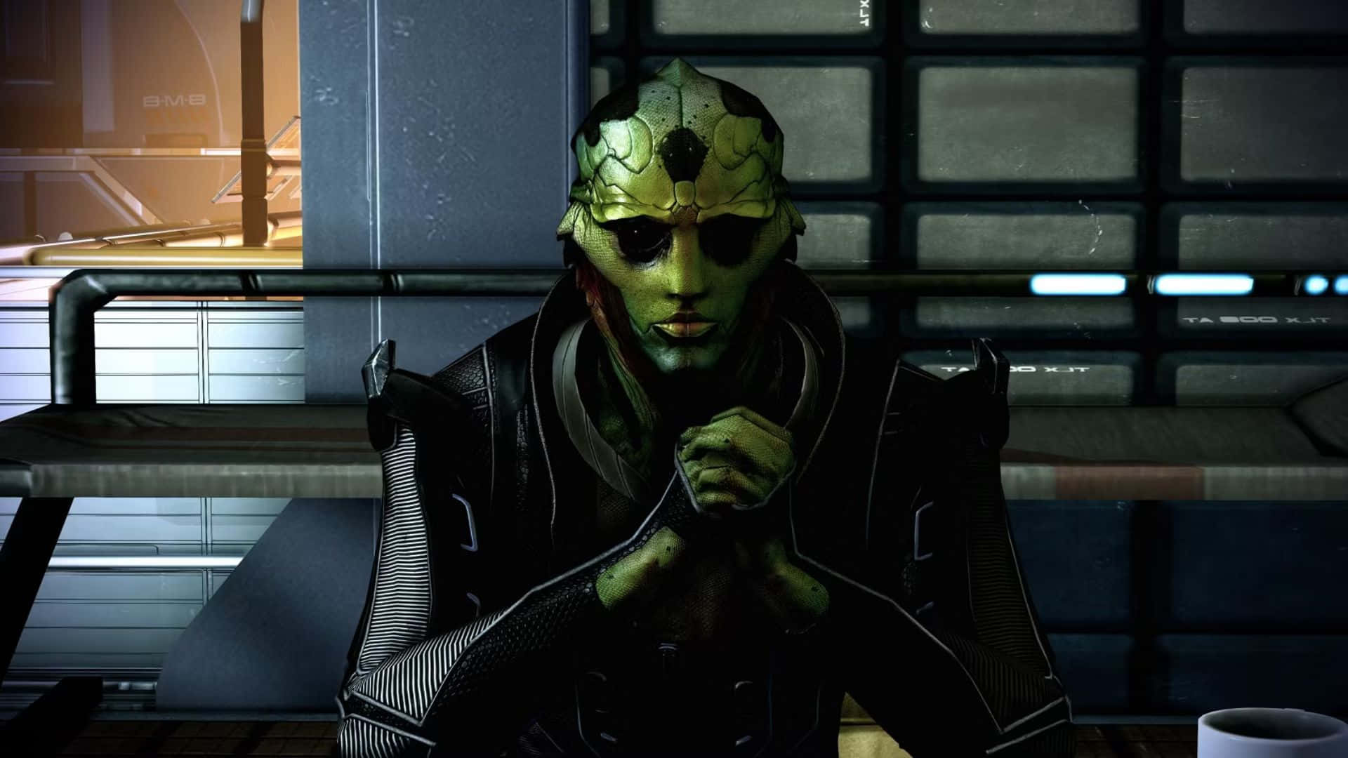 Thane Krios 桌布 壁紙 — 一個綠色皮膚的外星人戴著分段頭盔，坐在昏暗的未來房間裡，雙手合十，周圍是發光的面板和金屬表面。
