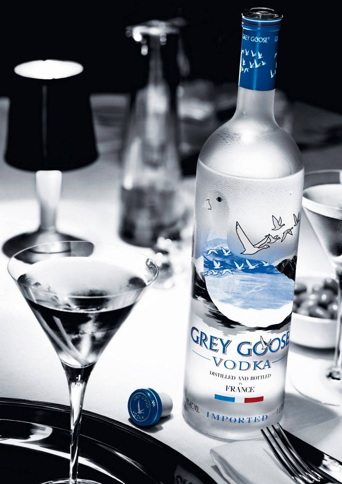 捕捉奢華 - Grey Goose伏特加 壁紙 — 一個時尚的灰色灰雁伏特加酒瓶，帶有藍色點綴，優雅地放在一個極簡的黑白餐桌佈置上，旁邊是一個馬提尼酒杯。