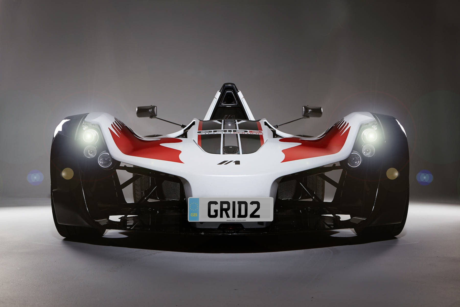 Grid 2 BAC Mono 賽車 壁紙 — 一輛時尚的白色和紅色賽車在攝影棚內亮著車頭燈，正面朝前。