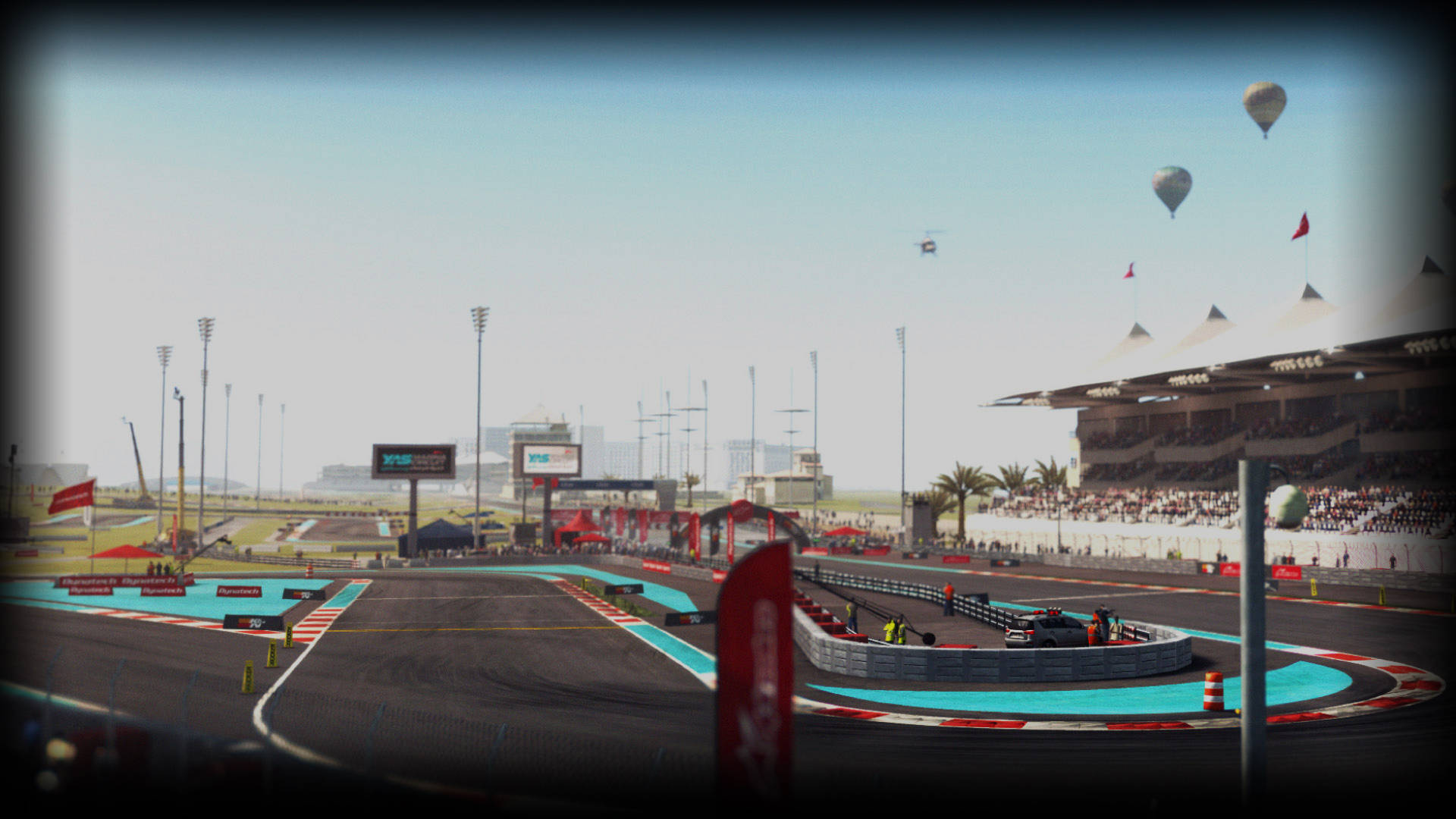 Grid Autosport 賽道與飛行氣球 壁紙 — 現代賽道的廣角視圖，設有藍綠色路緣和擠滿觀眾的看台，天空朦朧，熱氣球漂浮在上方。