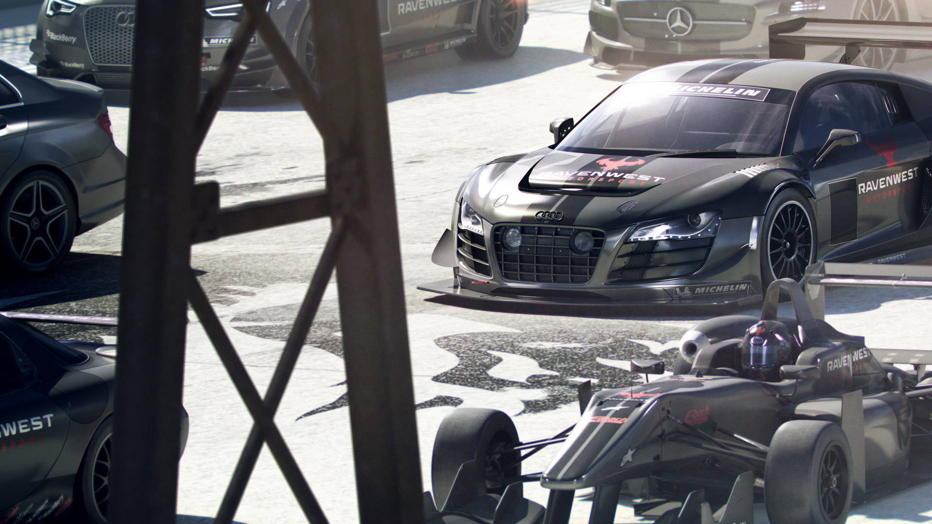 GRID Autosport 高速賽車風暴 壁紙 — 一架帶有 'Ravenwest' 品牌的時尚黑色奧迪 R8 賽車，在明亮的日光下與一級方程式賽車一起停在維修區車庫。