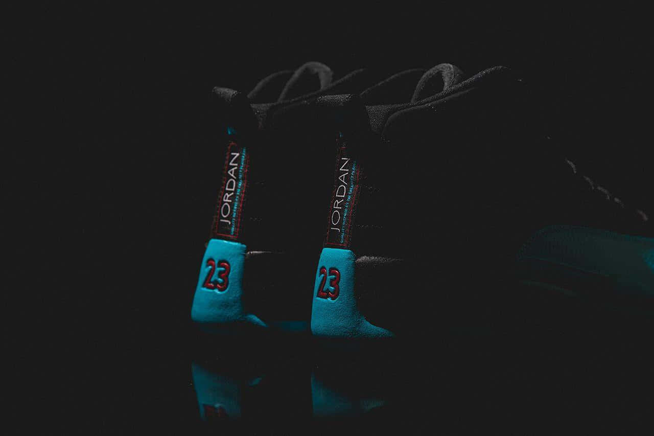 藍色喬丹GS 12「超級翡翠」 壁紙 — 一對黑色Jordan運動鞋，帶有發光的青色和紅色點綴，在漆黑的反射表面上脫穎而出。