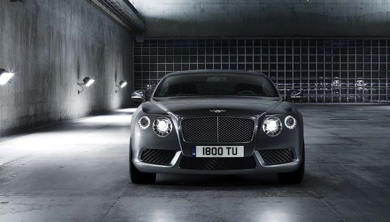 賓利大陸GT運動版 壁紙 — 一輛時尚的銀色賓利 Continental GT 在極簡混凝土車庫的聚光燈下閃閃發光，車庫牆壁帶有網格圖案。