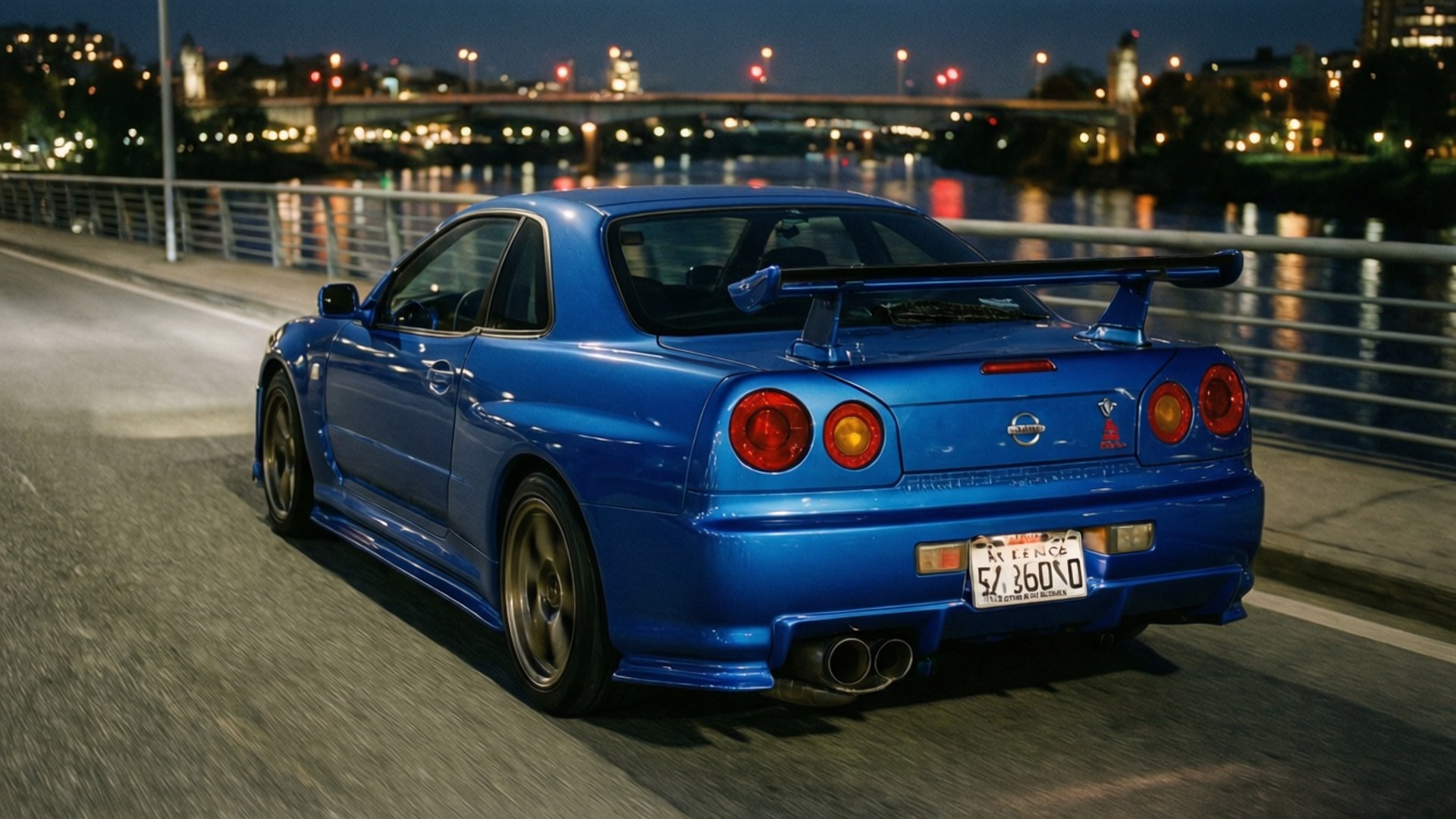 午夜GT-R 壁紙 — 一輛充滿活力的藍色日產Skyline R34在夜間沿著城市橋樑飄移，背後發光的城市燈光倒映在水面上。
