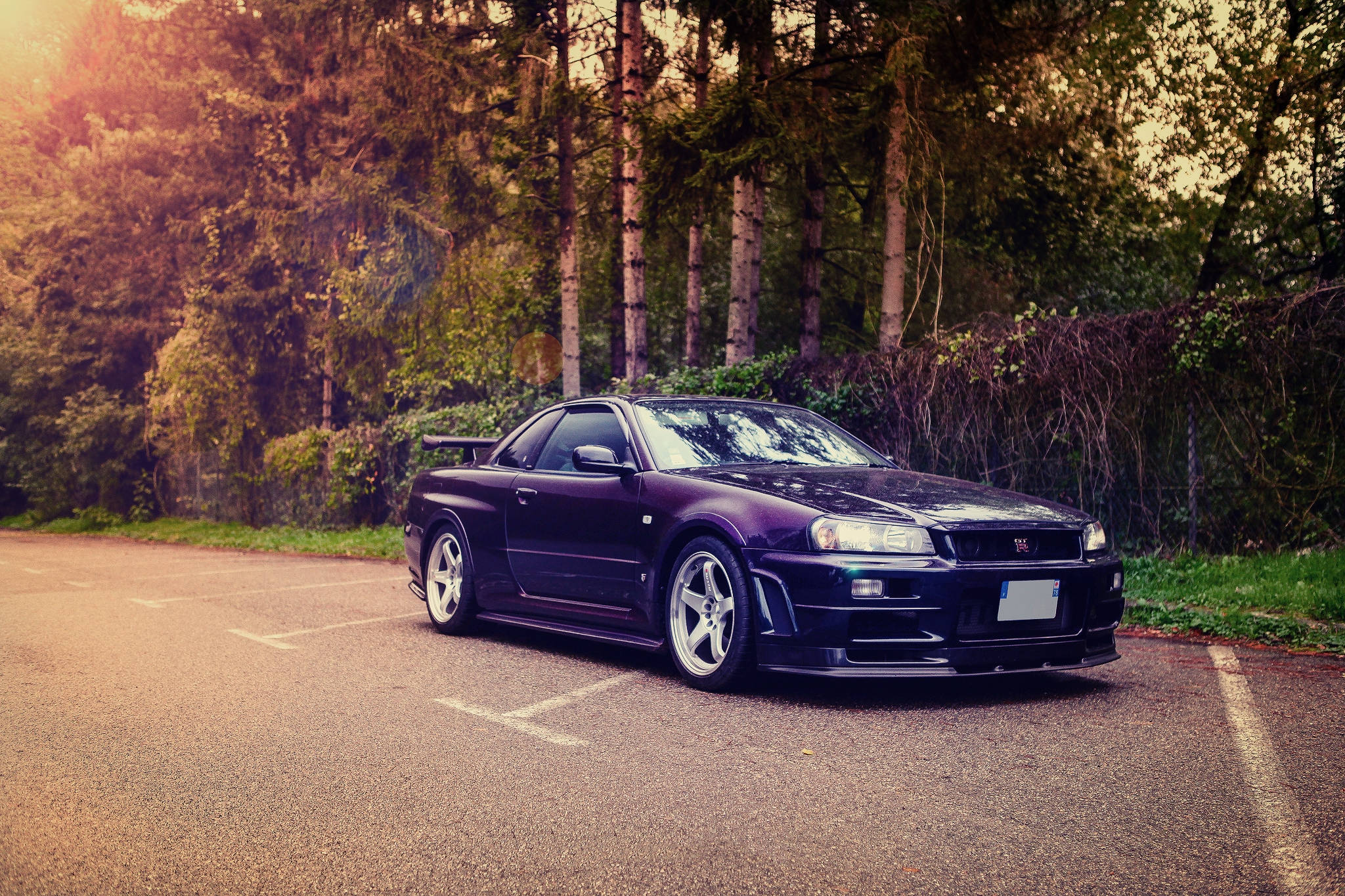 日產GT-R Skyline 壁紙 — 一架時尚的深紫色跑車停在森林環繞的道路上，沐浴在金色的夕陽光中。
