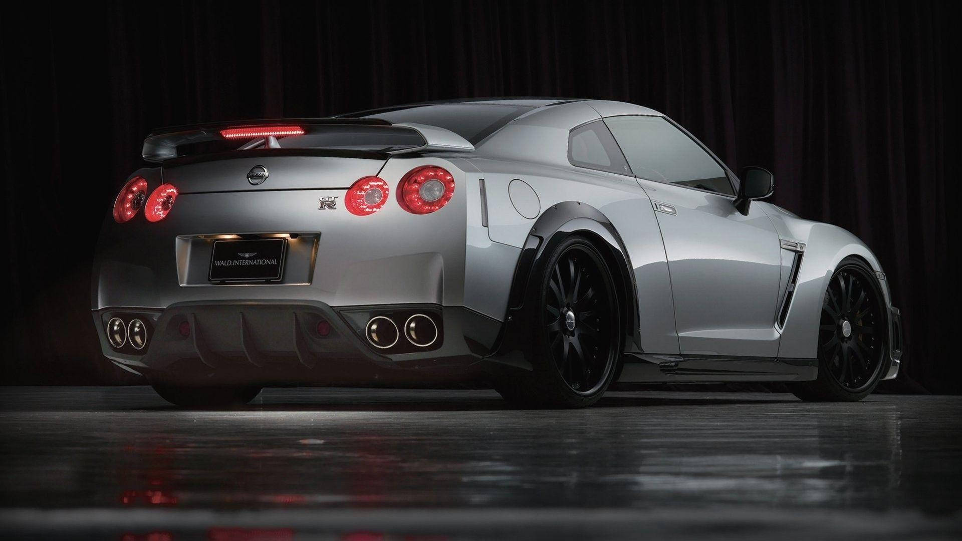 日產GT-R35全高清汽車壁紙 壁紙 — 一輛時尚的銀色日產GT-R跑車，帶有發光的紅色尾燈，在帶有反射地板的黑暗舞台上展示。