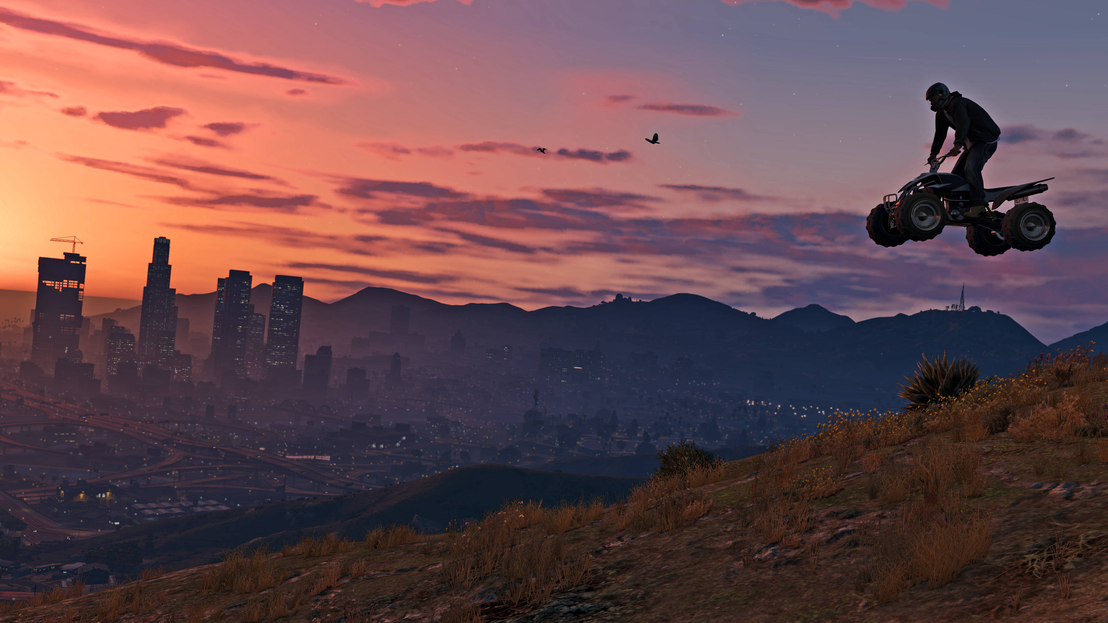 GTA V ATV 空中飛躍 壁紙 — 一名騎手在日落時分駕駛ATV飛越山坡，遠處是廣闊的城市天際線和山脈。