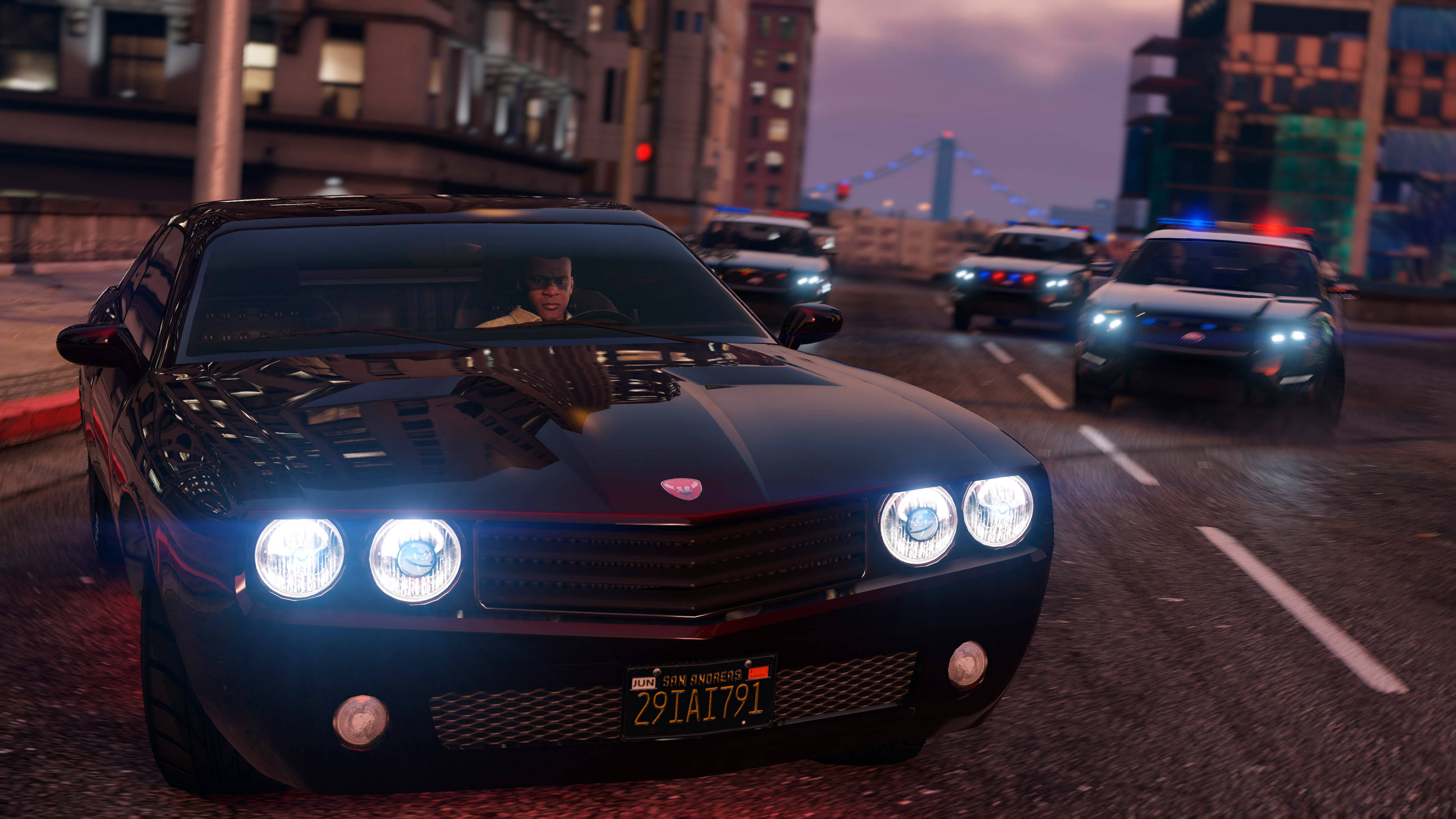 GTA V 富蘭克林被警察逮捕 壁紙 — 一輛黑色肌肉車亮著明亮的車頭燈，在黃昏時分被警車追捕，高速駛過城市街道。