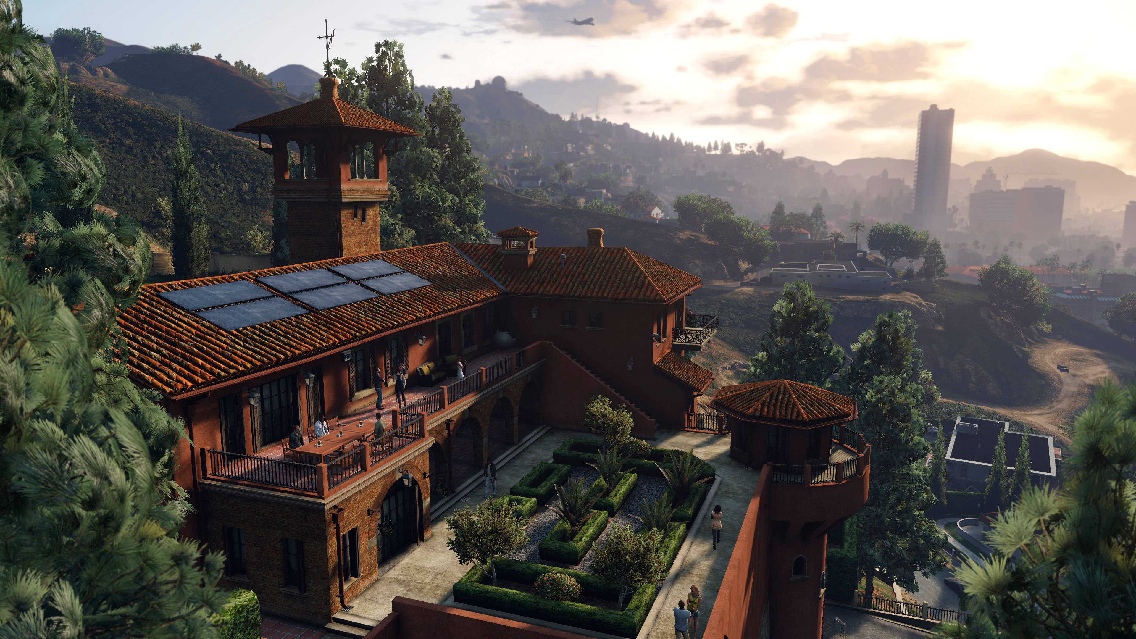 GTA V 花花公子莊園 壁紙 — 一座寬敞的地中海風格別墅，擁有陶土屋頂和太陽能板，坐落在山頂上，俯瞰著金色時刻朦朧的城市景觀。