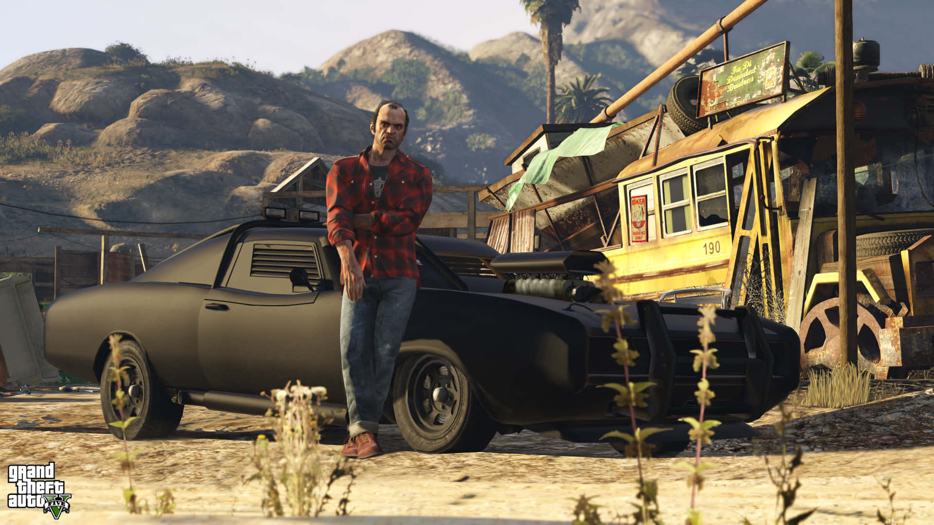 GTA 中男子倚靠汽車背景 壁紙 — 一個穿著紅色格仔恤衫的男人，在塵土飛揚的沙漠廢車場，靠著一輛黑色肌肉車，背景有山。