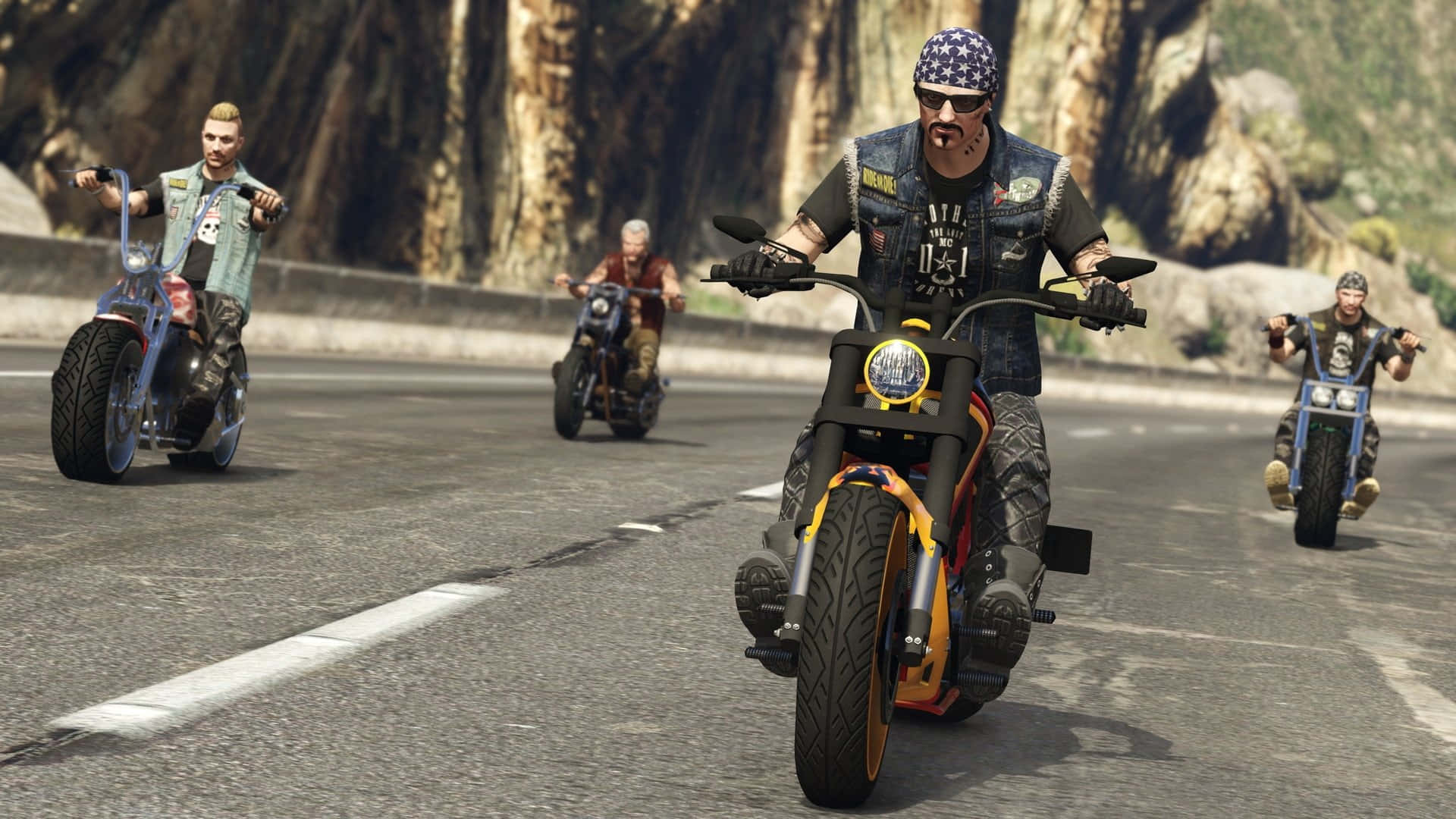 GTA中摩托車團體出遊 壁紙 — 四位身穿皮背心的電單車手，在陽光明媚、有岩石峭壁的山區高速公路上騎著訂製電單車。
