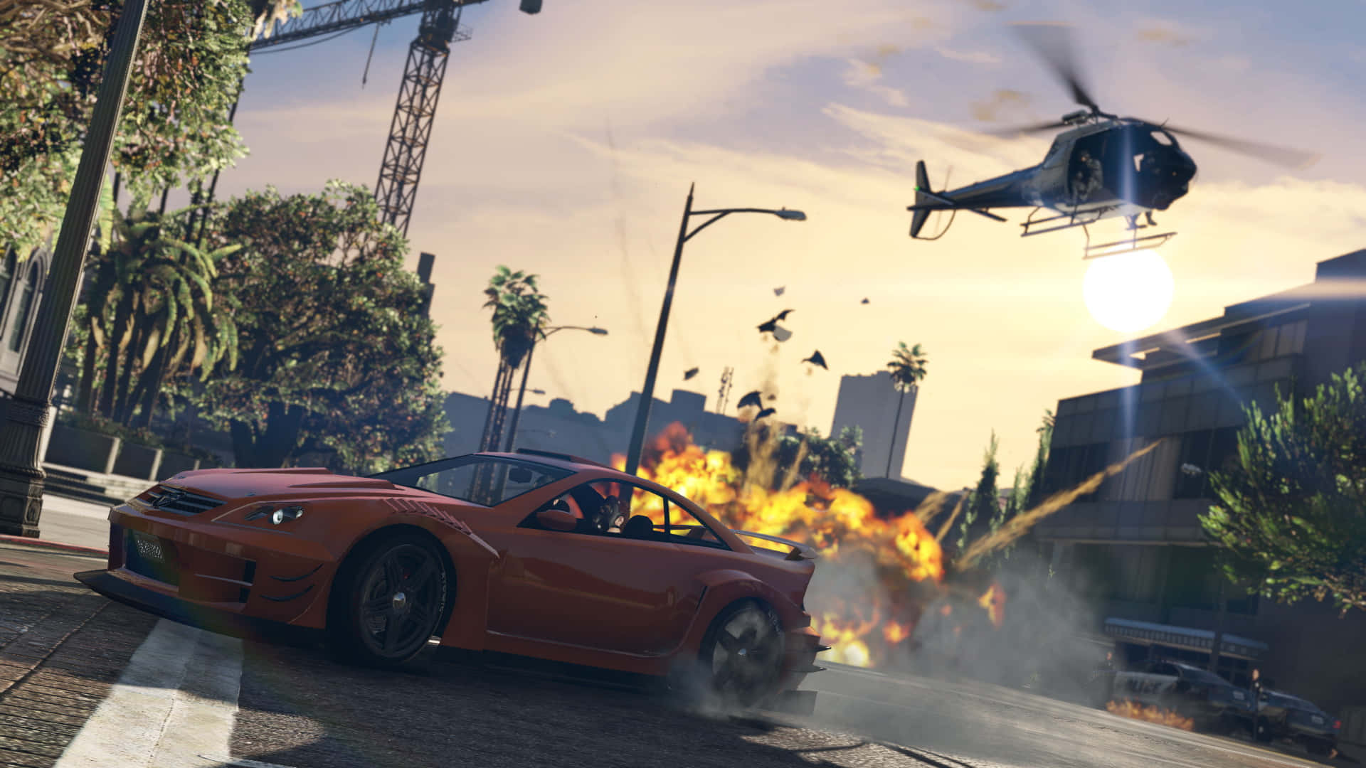 GTA中的城市混亂場景 壁紙 — 一輛火熱的橙色跑車在城市的街道上飛馳，身後發生爆炸，一架直升機在日落時分從頭頂飛過。