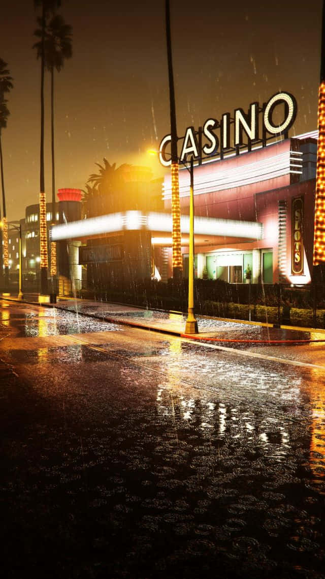 GTA五賭場背景 壁紙 — 一個雨夜場景顯示一棟燈火通明的賭場建築，棕櫚樹和濕漉漉的人行道反射著霓虹燈光。