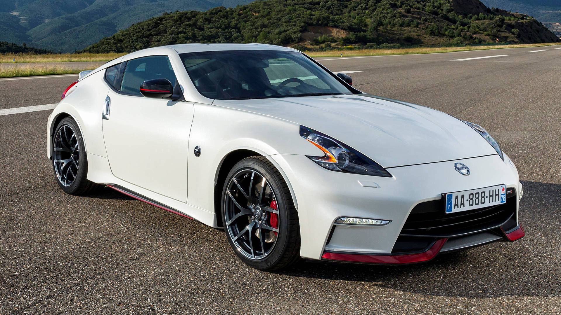 尼桑GTR 370z Nismo 壁紙 — 一輛時尚的白色日產370Z跑車帶有紅色點綴，停在瀝青路上，背景是綠色山丘。