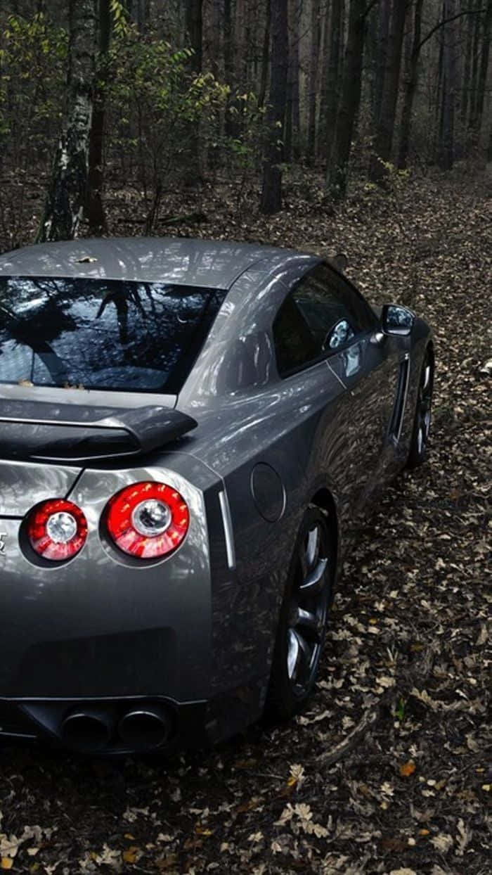 銀色 GTR R35 林間停泊 壁紙 — 一輛時尚的銀色跑車，帶有發光的紅色尾燈，停在落葉覆蓋的森林地面上。