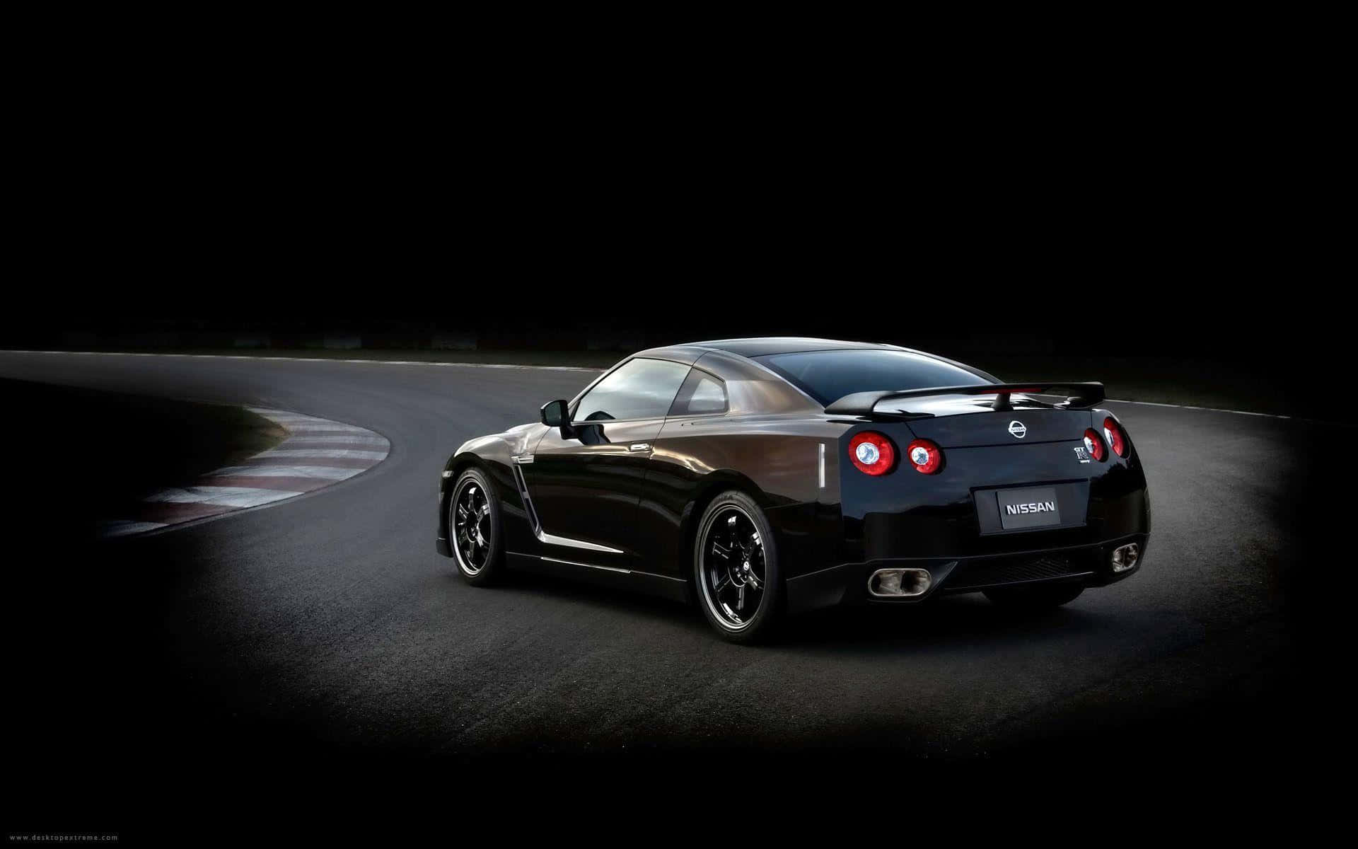 日產GTR桌面壁紙 壁紙 — 一架型格黑色日產GT-R跑車在戲劇性聚光燈下，於黑暗賽道彎位滑行。
